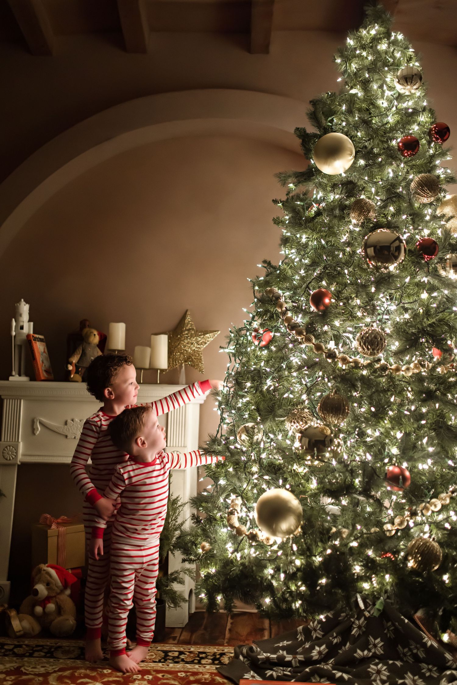 Children in striped pajamas admiring a glowing Christmas tree decorated with gold ornaments.