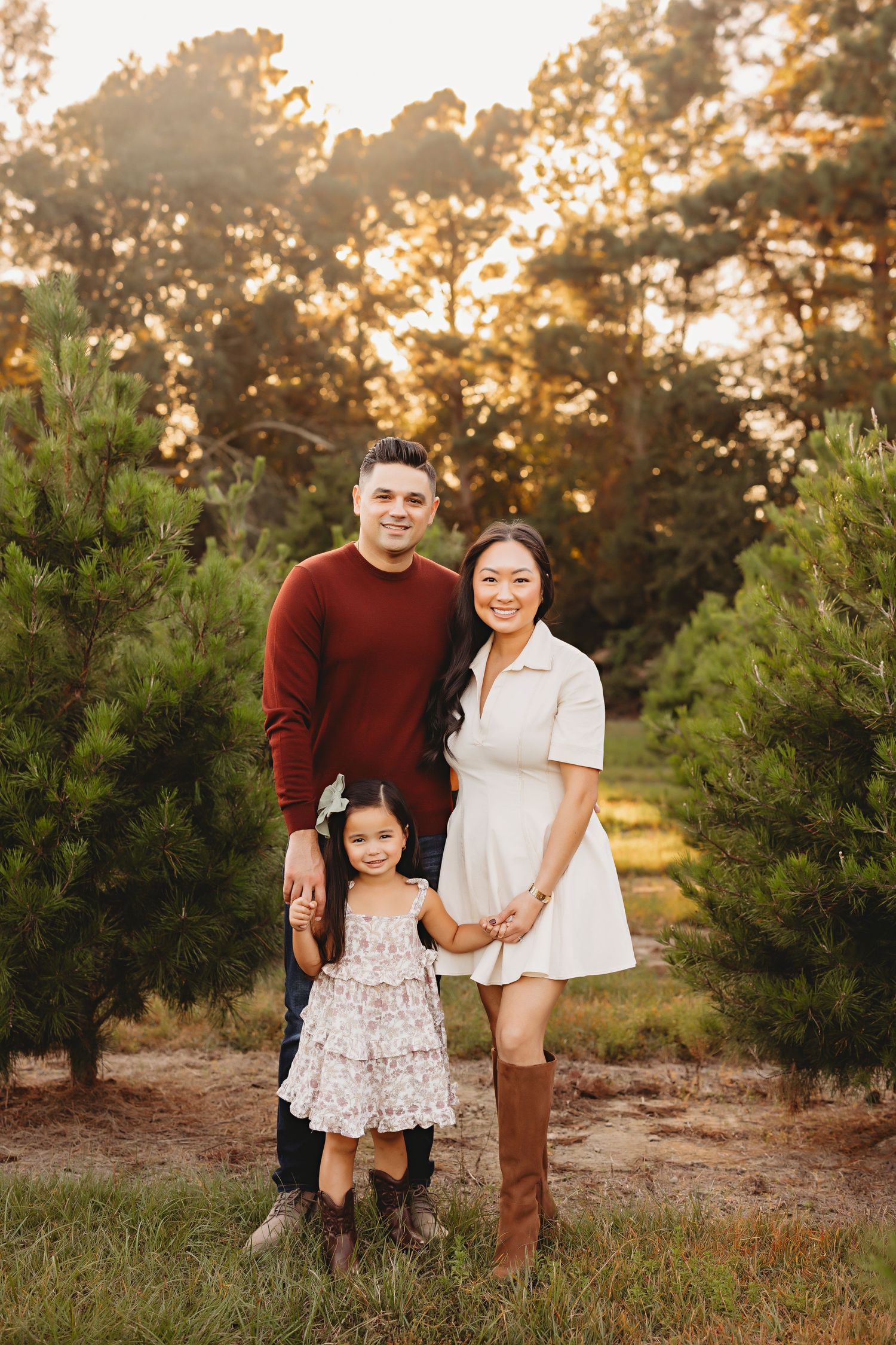 A family poses between evergreen trees during sunset at a Christmas tree farm.