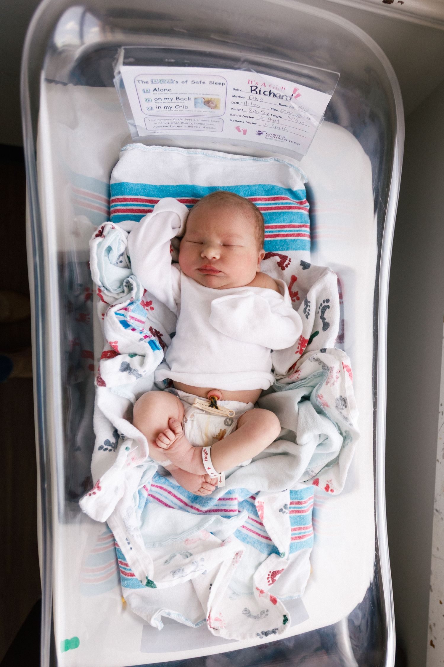 Newborn baby sleeping peacefully in hospital bassinet with striped blanket for Fresh 48 session.