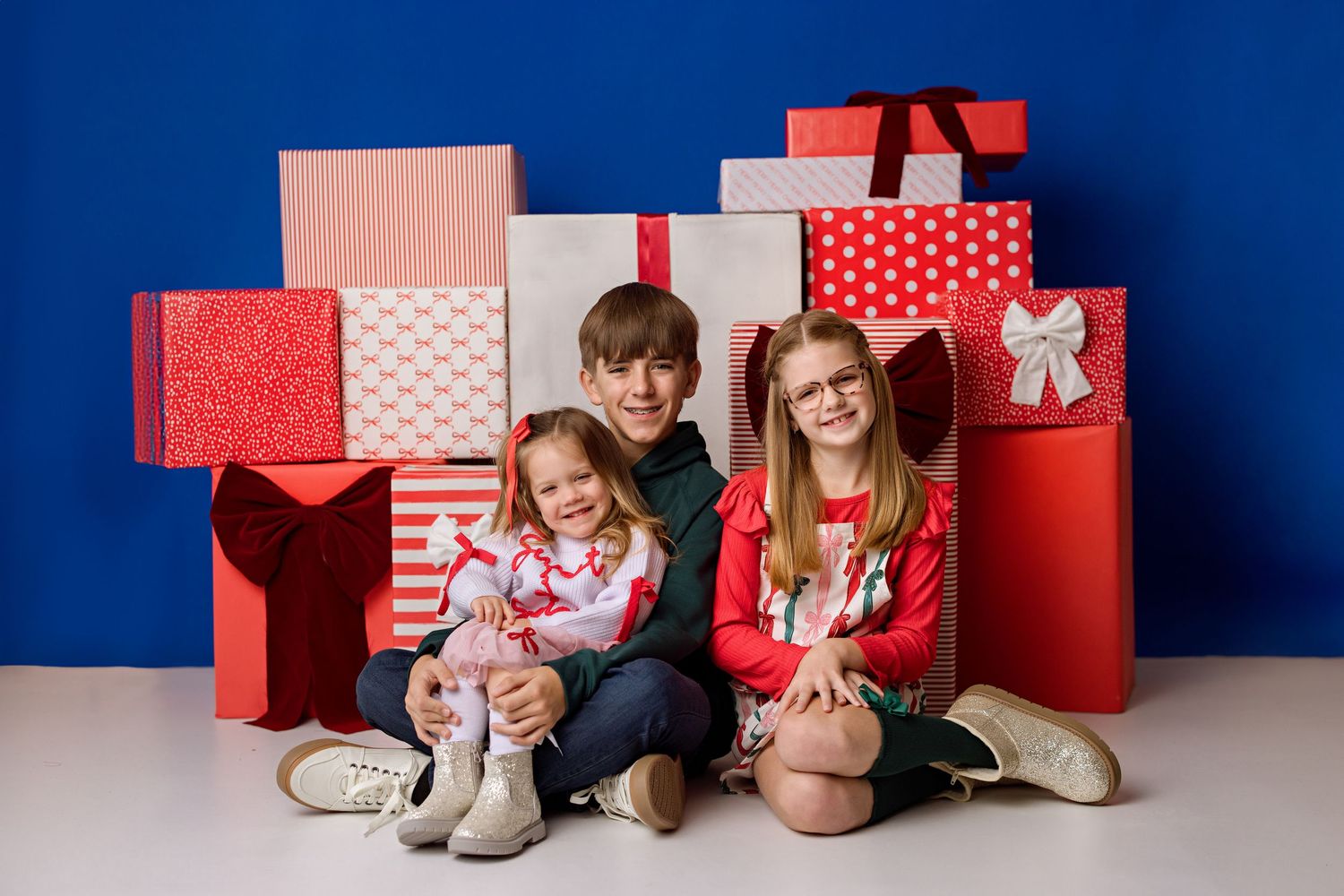 A series of holiday family portraits against a blue wall with red and white polka dot wrapped Christmas presents.