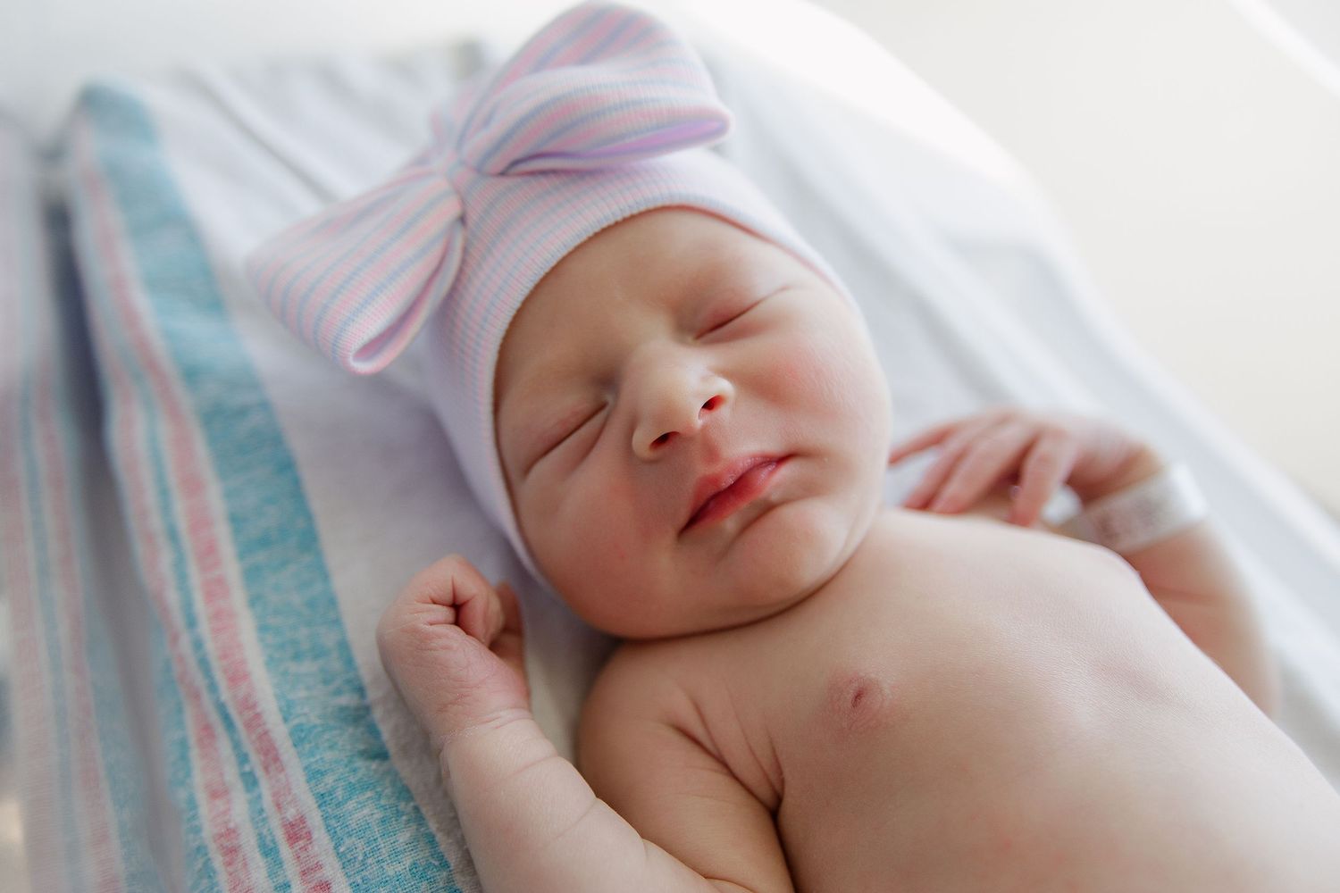 Newborn wearing pink cap sleeping peacefully on white bedding during Fresh 48 session in Beaumont hospital.