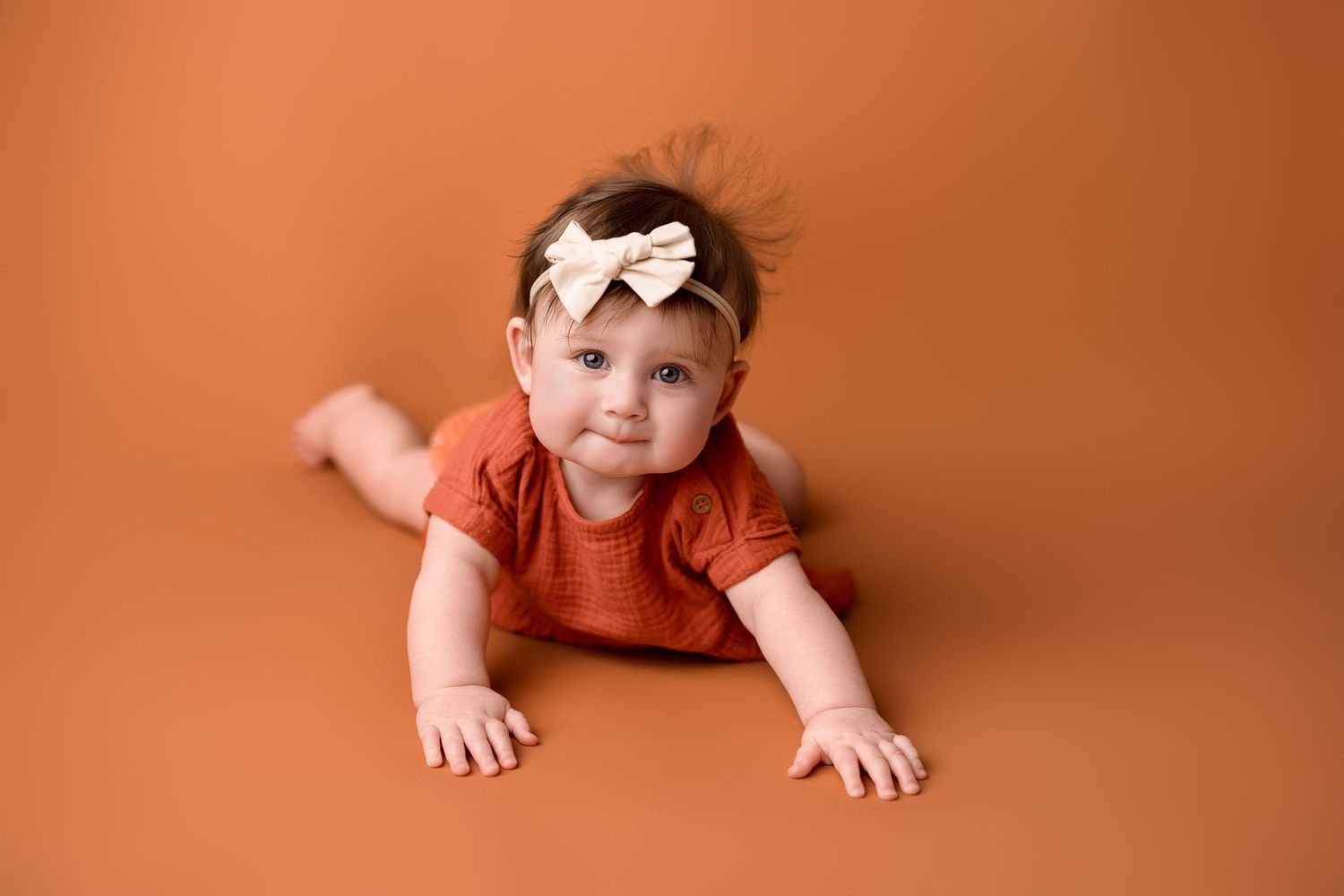 A baby in a pink outfit crawls across a warm orange backdrop in a series of progressive movement shots.