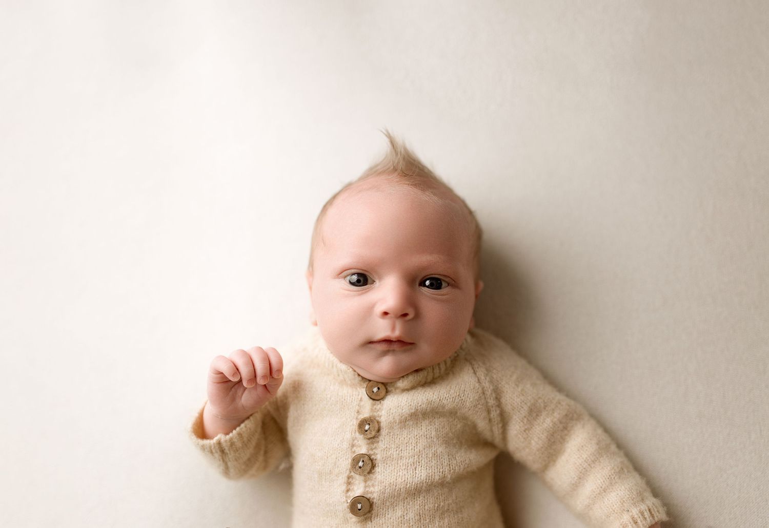 A baby in a cream-colored knit sweater lying on a beige blanket.
