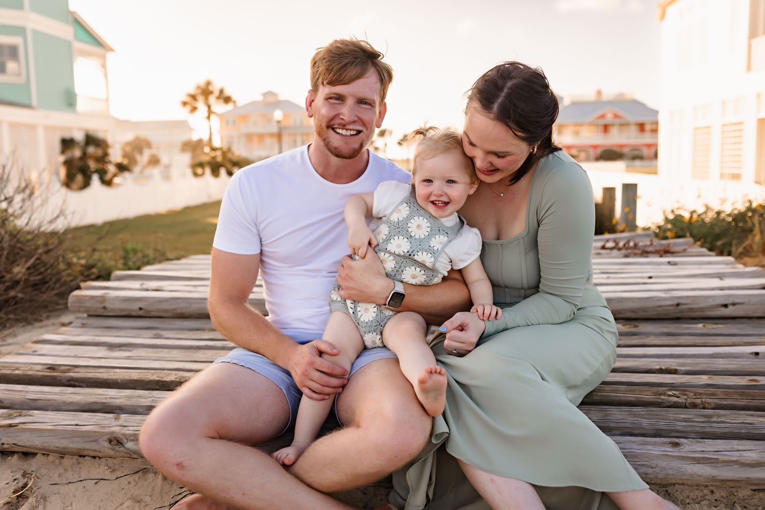 A family shares a tender moment together while sitting on wooden boards near the beach.
