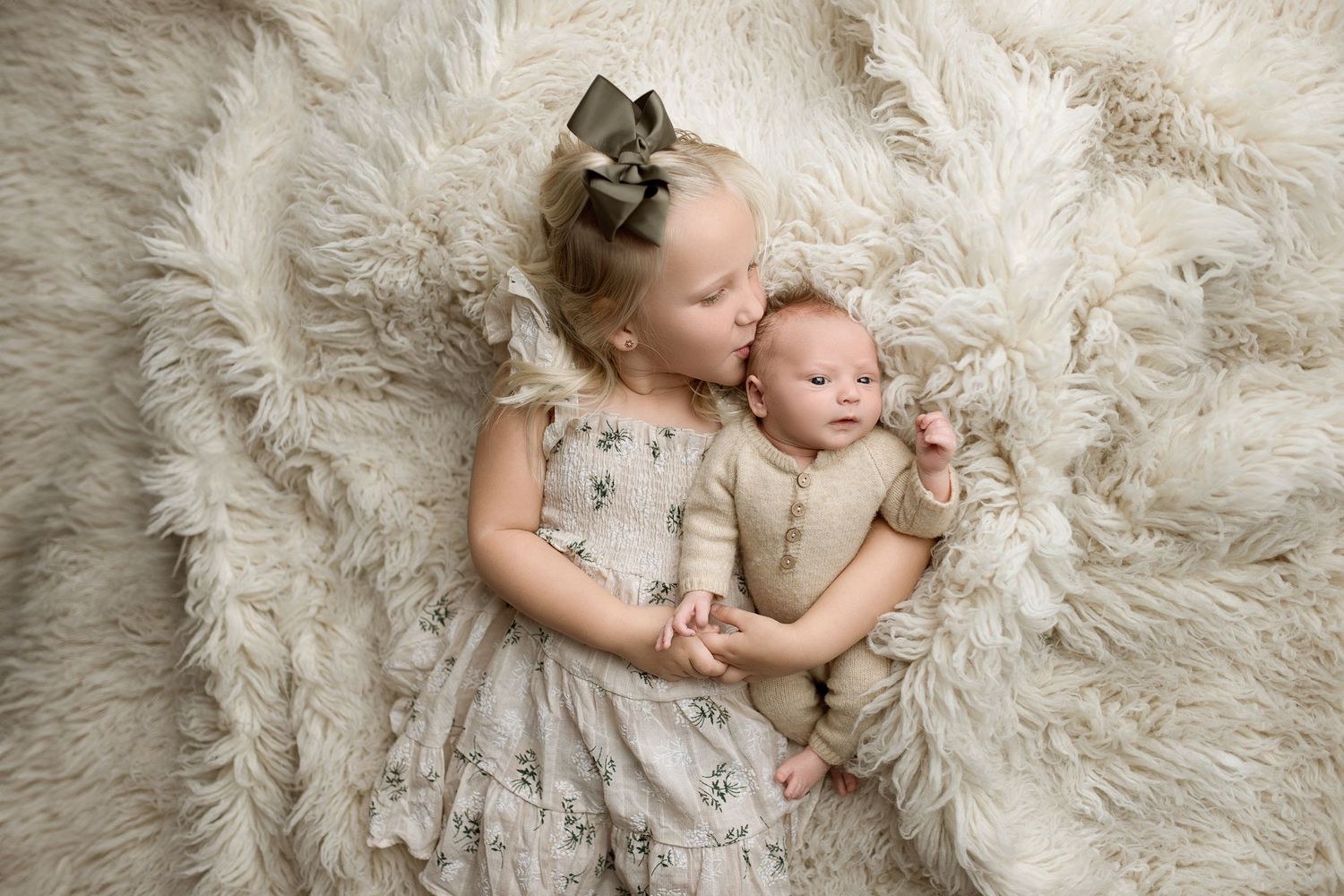 Baby lying on soft white fluffy rug during professional newborn photography session.