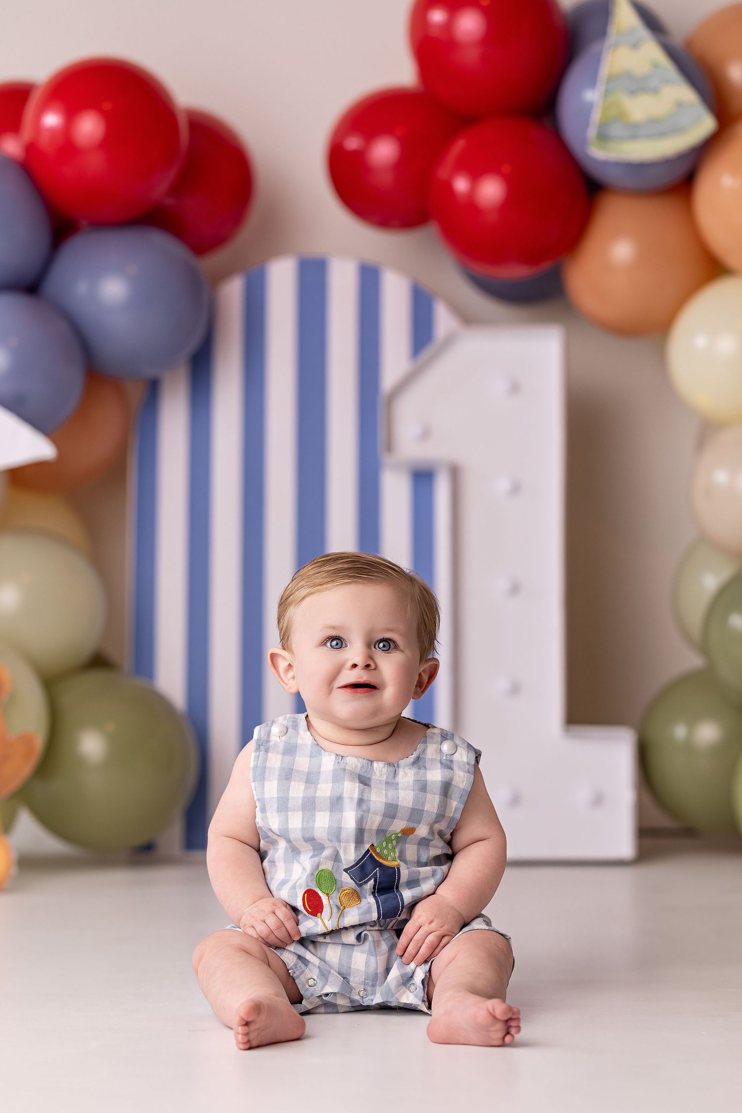 First birthday party setup with colorful balloon arch and blue and white striped number one backdrop.