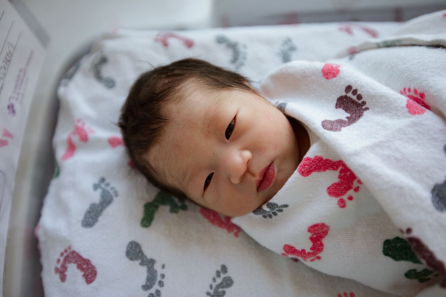 Sleeping infant swaddled in white blanket decorated with colorful footprint designs.