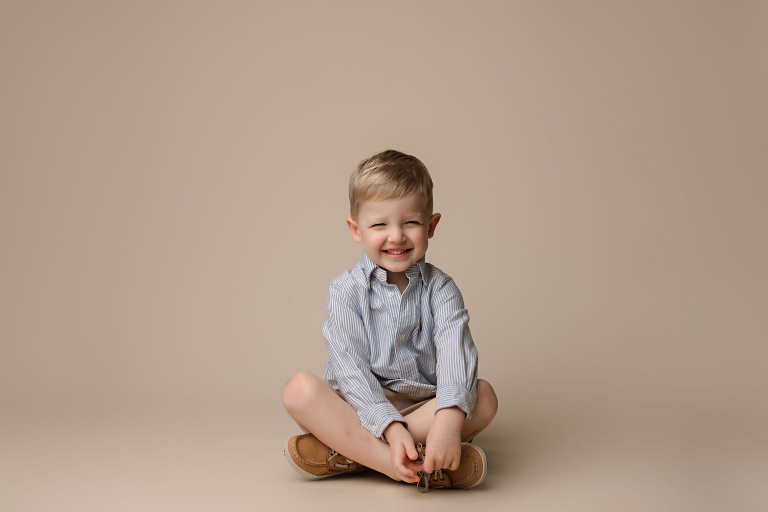 Child in casual attire during minimalist portrait session against neutral backdrop.