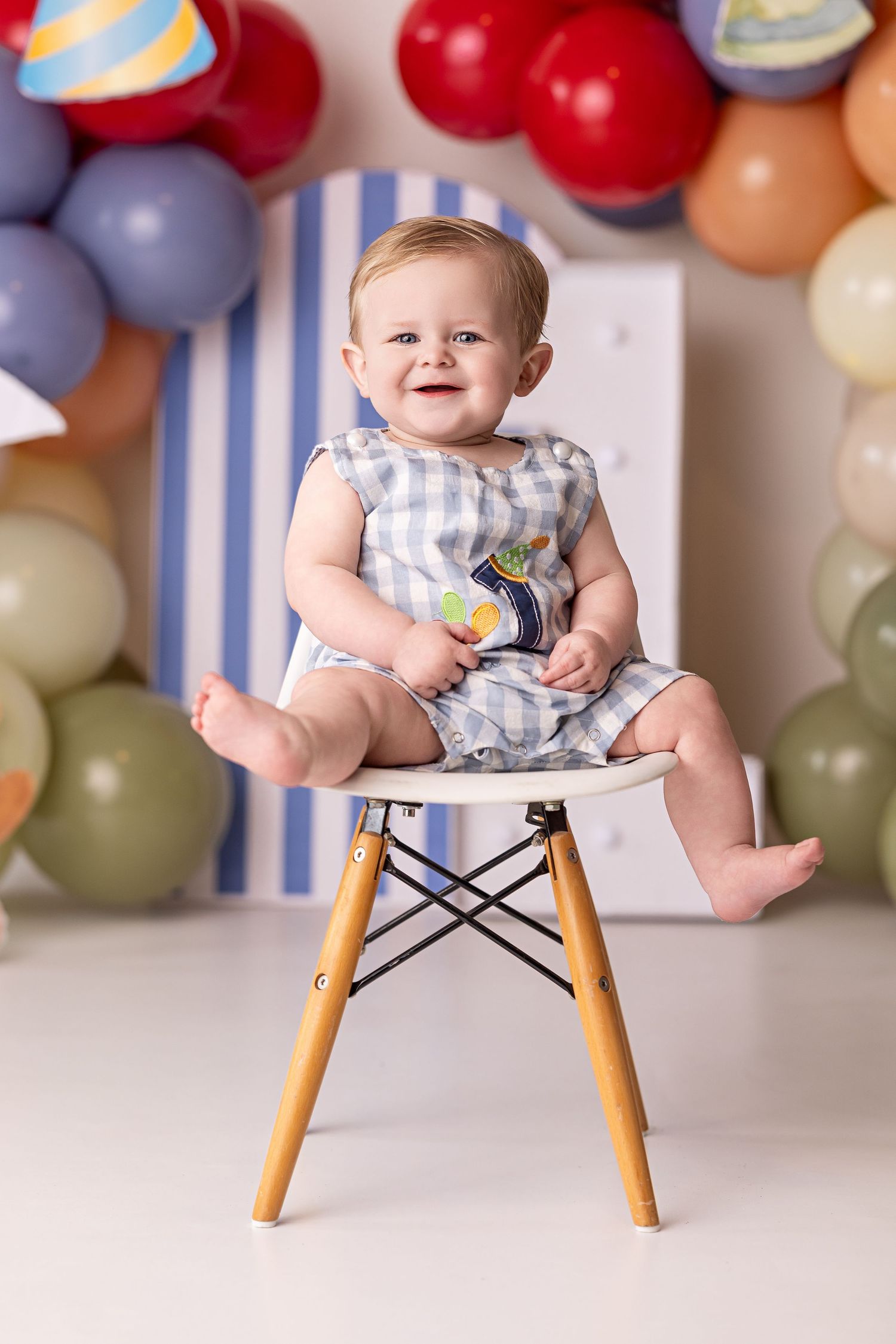 Colorful balloon backdrop with a wooden chair setup for a first birthday photoshoot celebration.