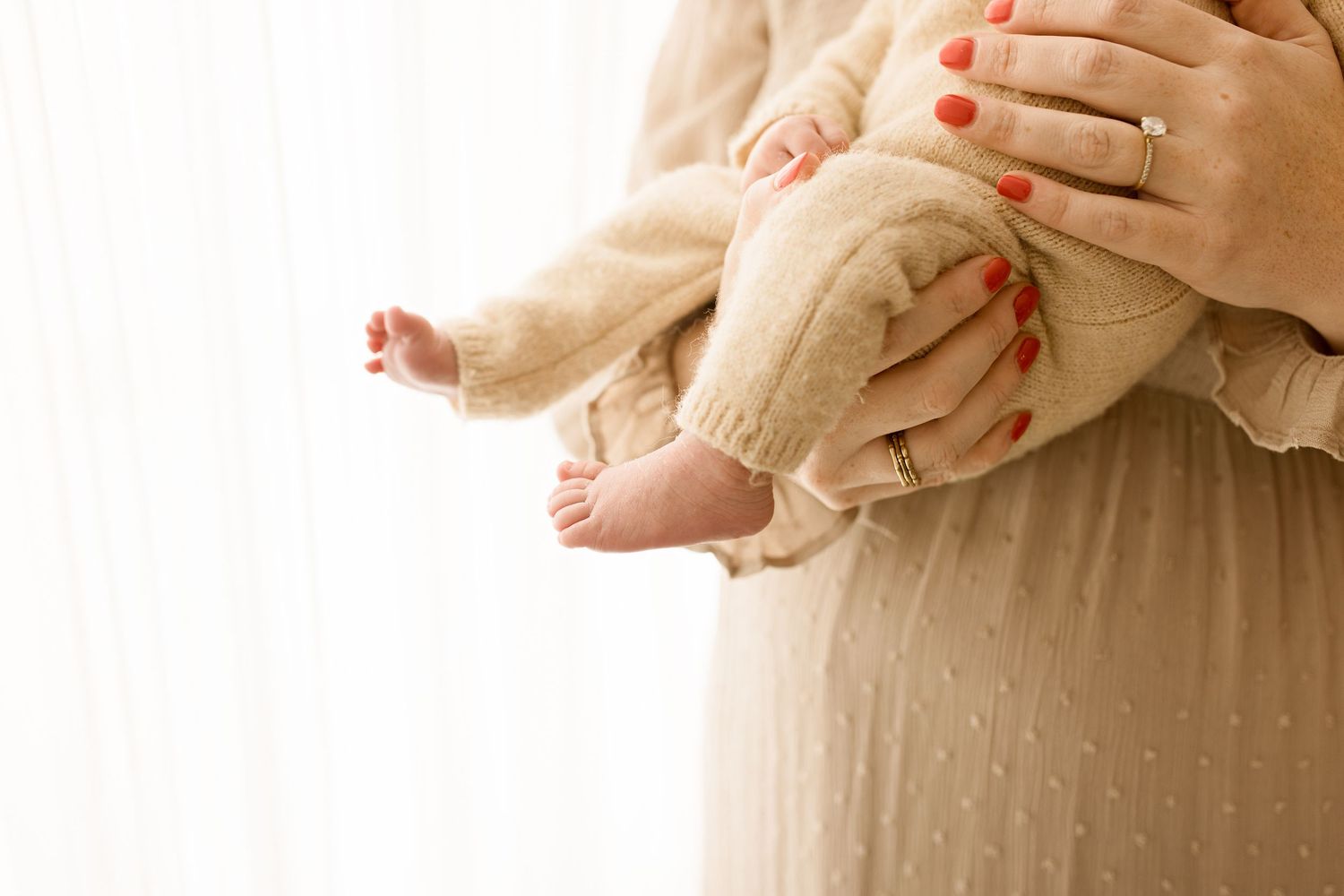 Newborn baby wrapped in beige knit blanket lying on textured white bedding.