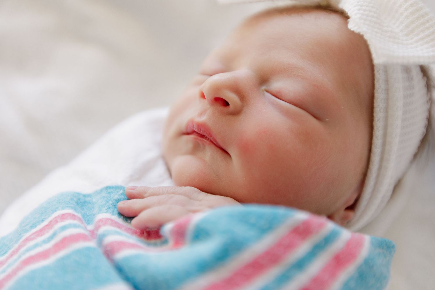 Close up of a sleeping newborn wearing a white cap and blue striped blanket during Fresh 48 session in Beaumont hospital.