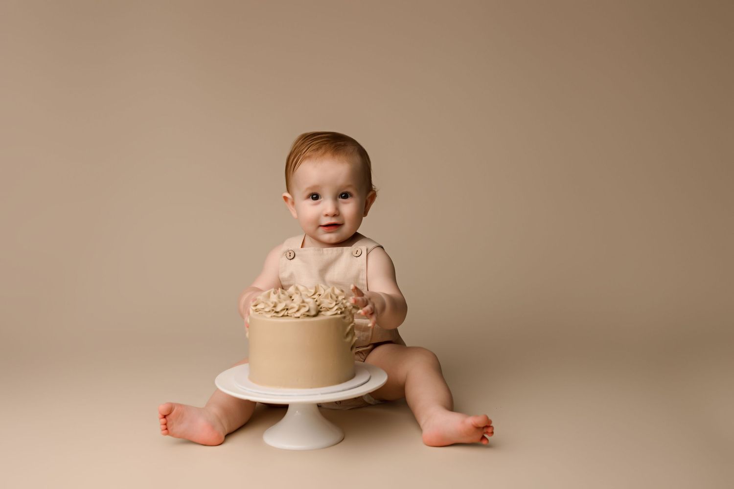 Studio portrait with beige cake on pedestal against neutral backdrop.
