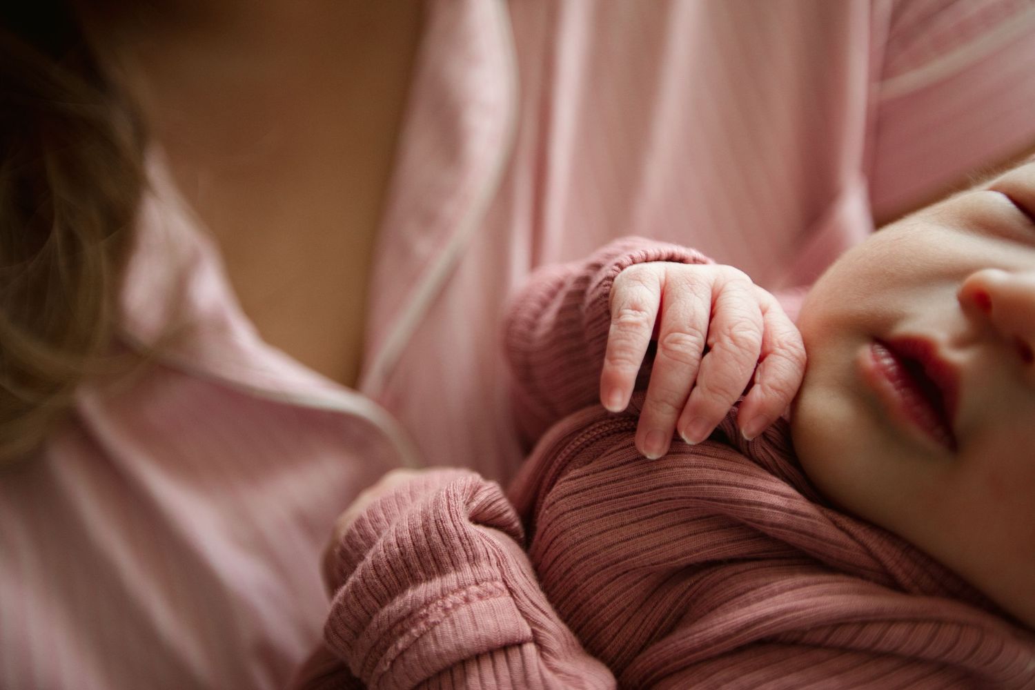 Close-up shot of a baby in pink clothing holding hands with someone.