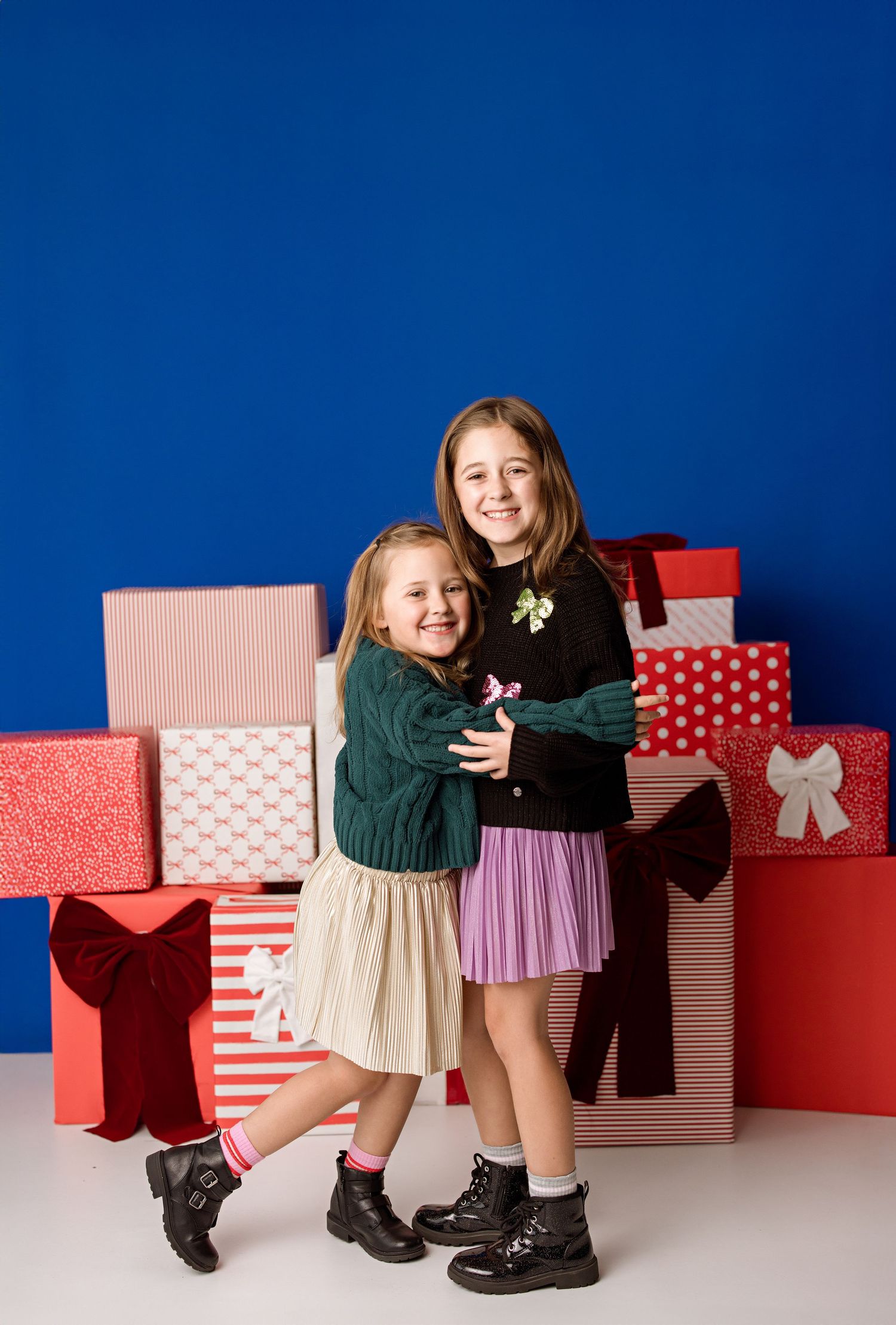 Two people pose with festive red and white wrapped Christmas presents against a deep blue background.