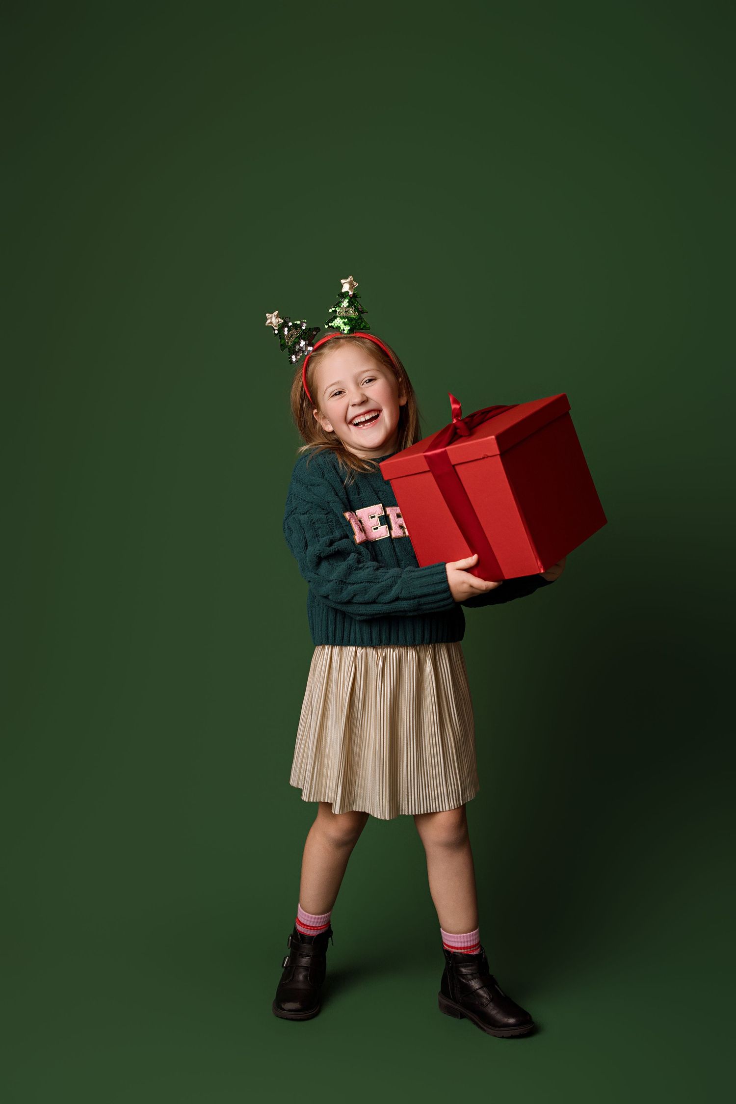 A sequence of four festive holiday photos showing a child in a dress holding and playing with a red gift box.
