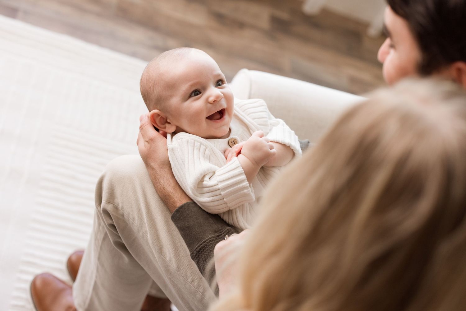 A happy baby laughs while being held up in the air during a tender moment with family.