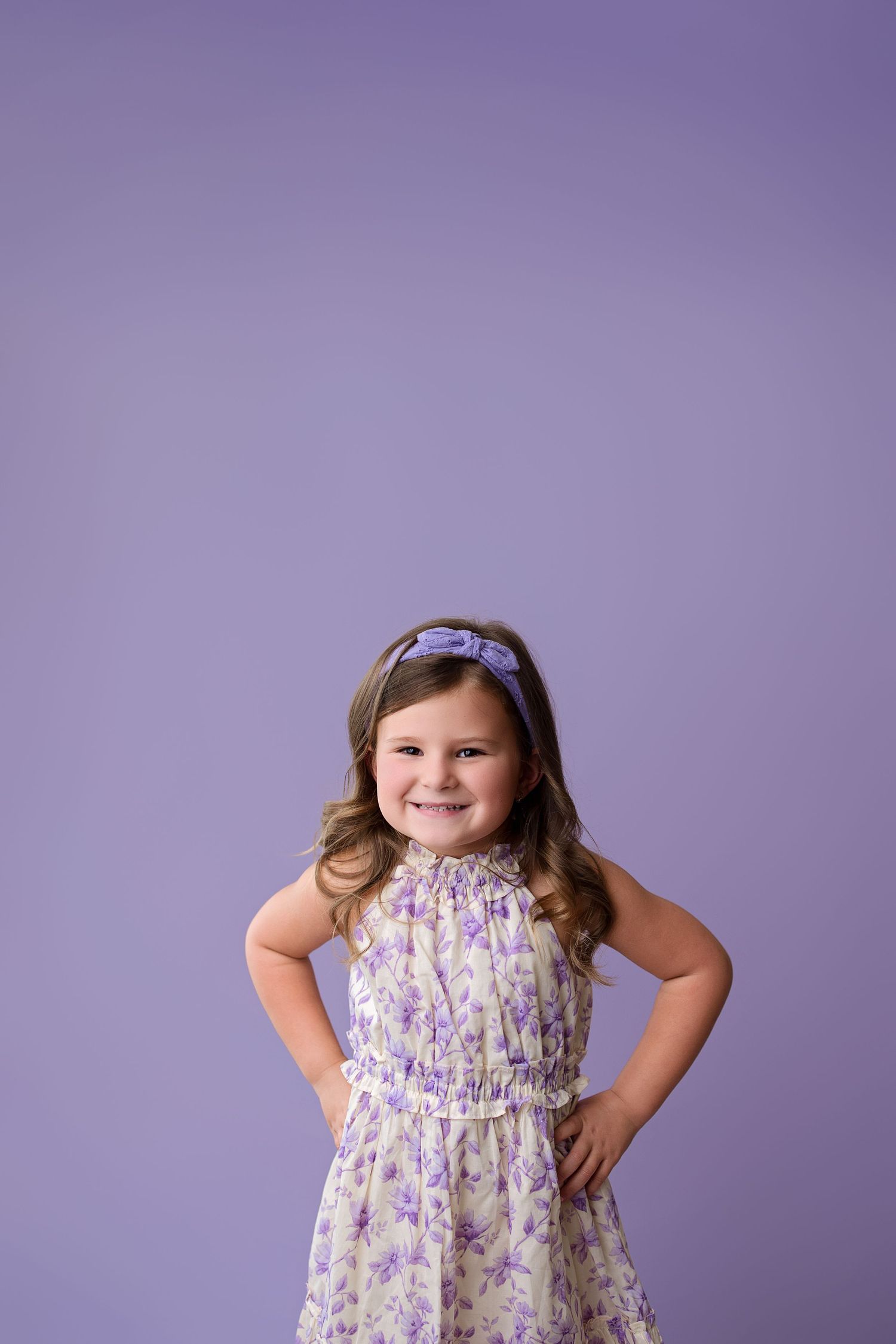 A child poses playfully in a floral dress against a purple backdrop in three similar expressions.