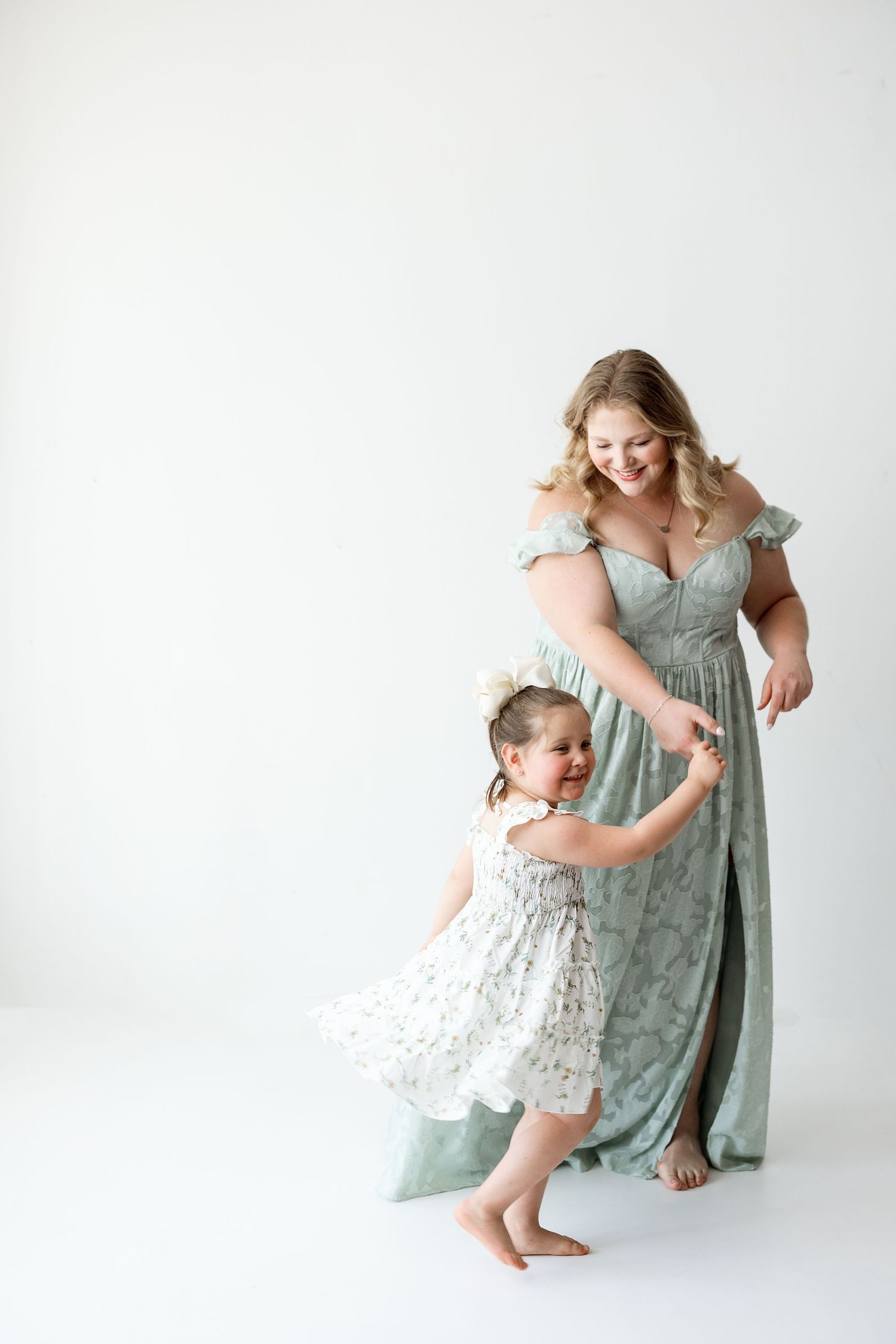Mother and toddler dancing together in matching mint green dresses against white background.