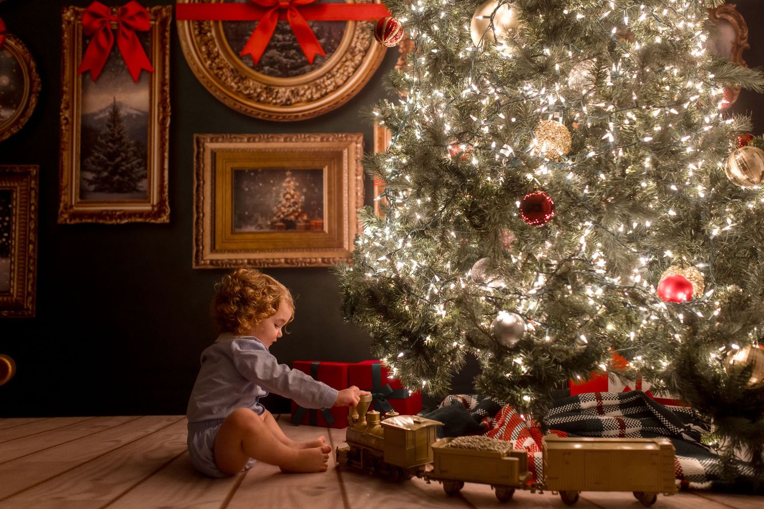 A child sits in front of a brightly lit Christmas tree opening presents in a cozy living room setting.