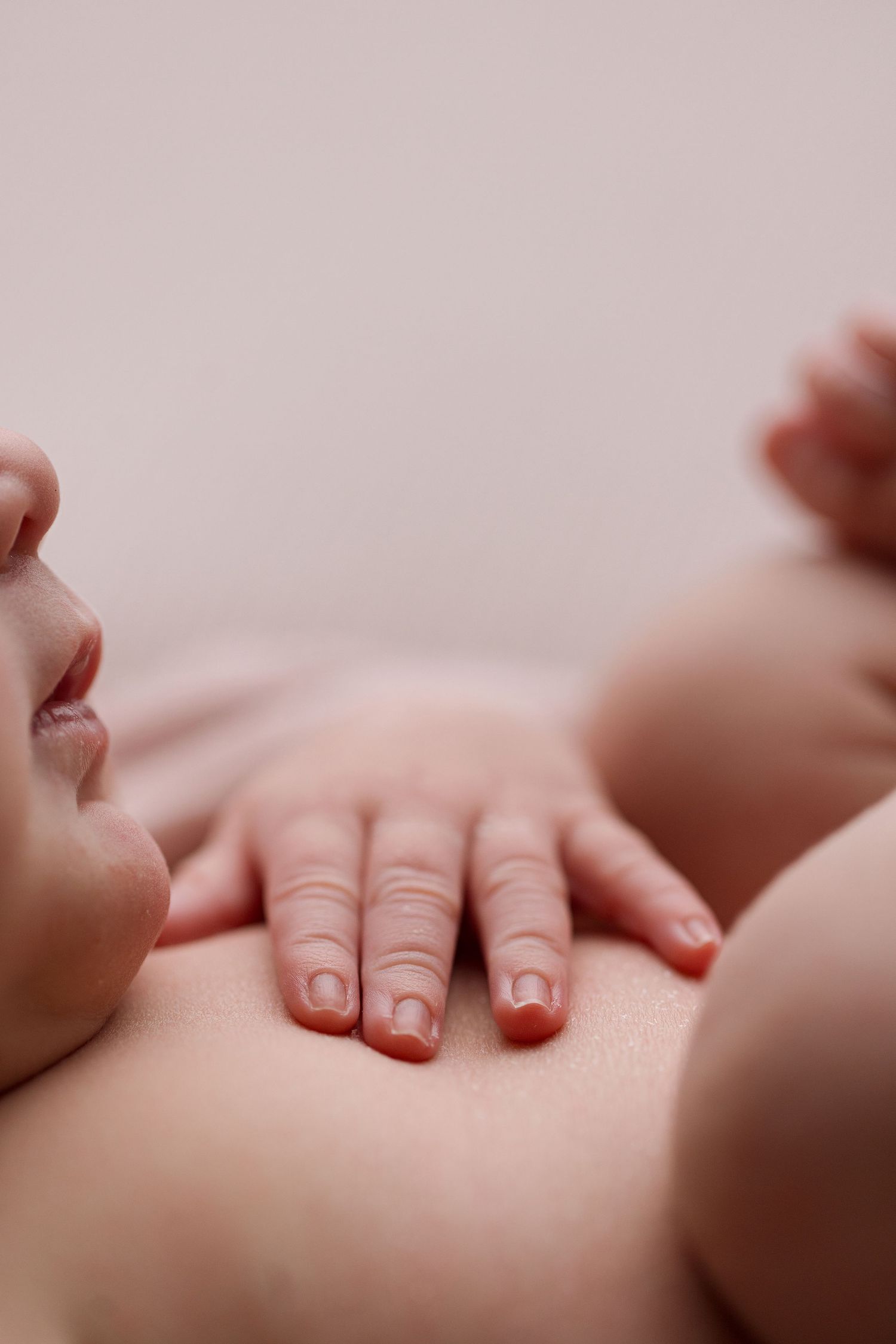 Close-up of tiny baby fingers and toes showing delicate newborn details against soft pink background.