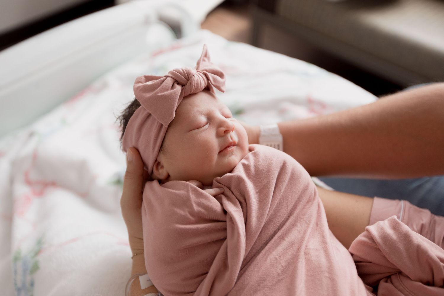 A baby dressed in a pink onesie lies peacefully on a soft blanket while sleeping.