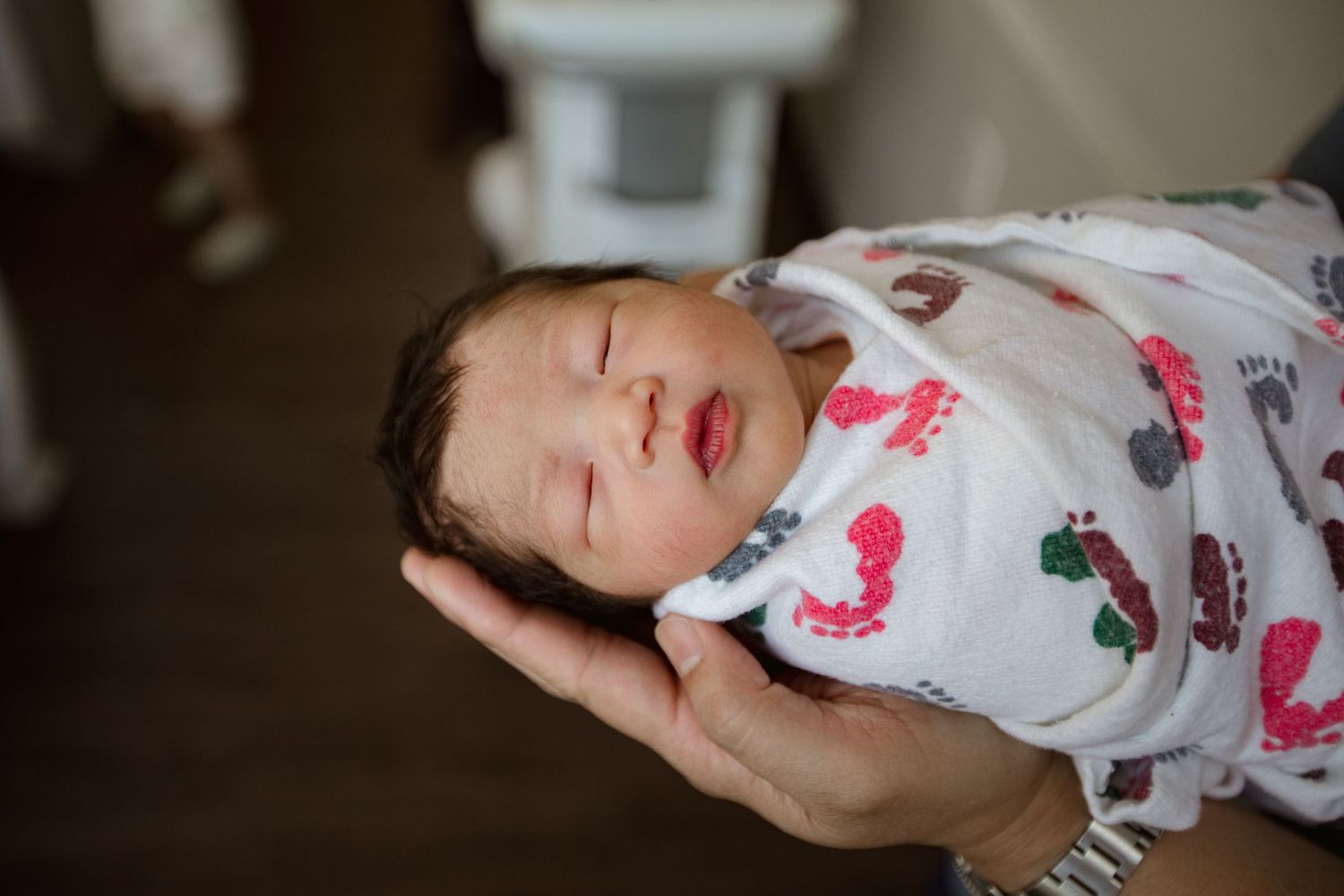 Peaceful sleeping newborn wrapped in white footprint-patterned blanket.