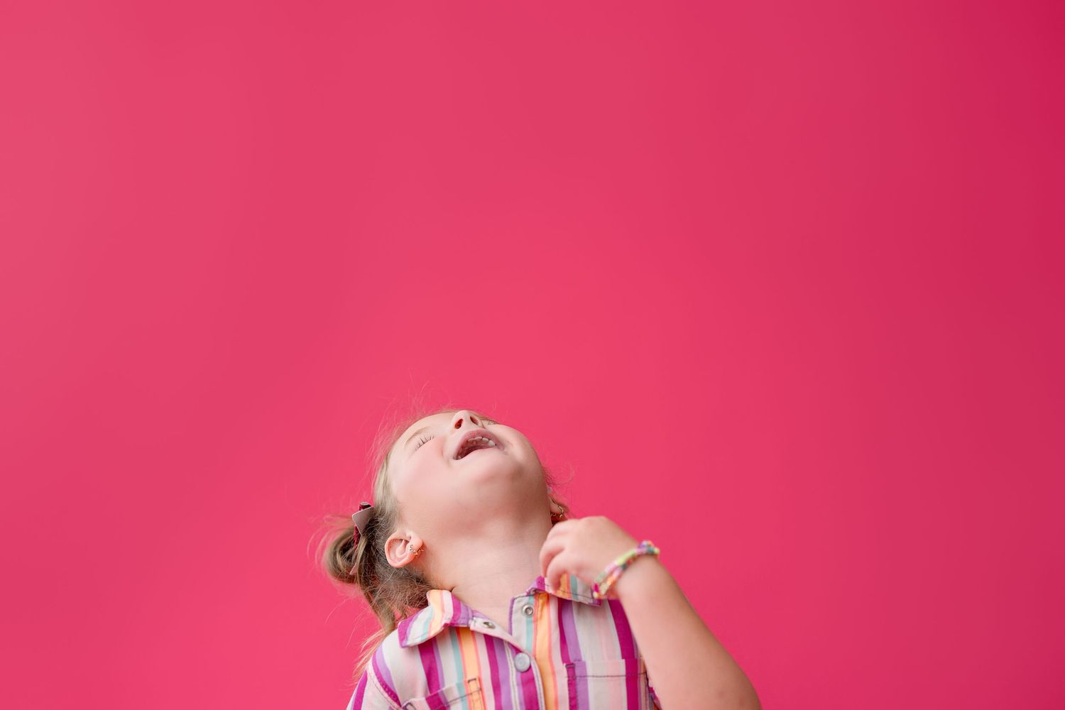Child laughing and playing against vibrant pink background showing pure joy and energy.