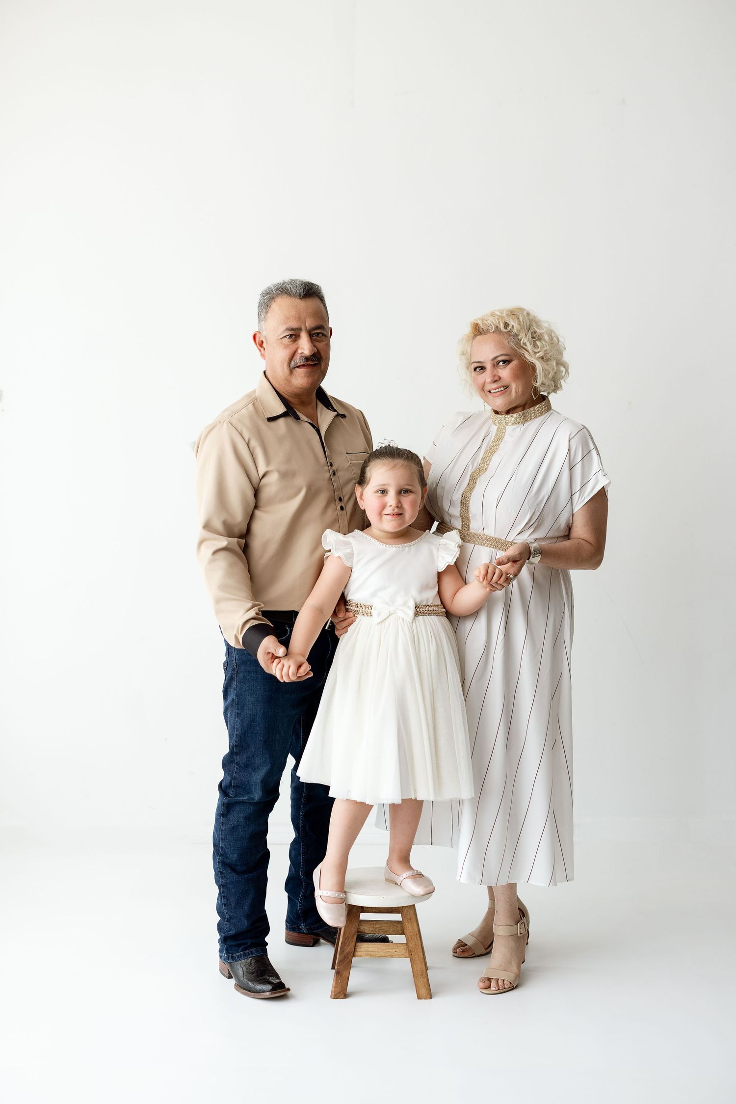 Three generations of family members pose together in white outfits against a bright studio background.