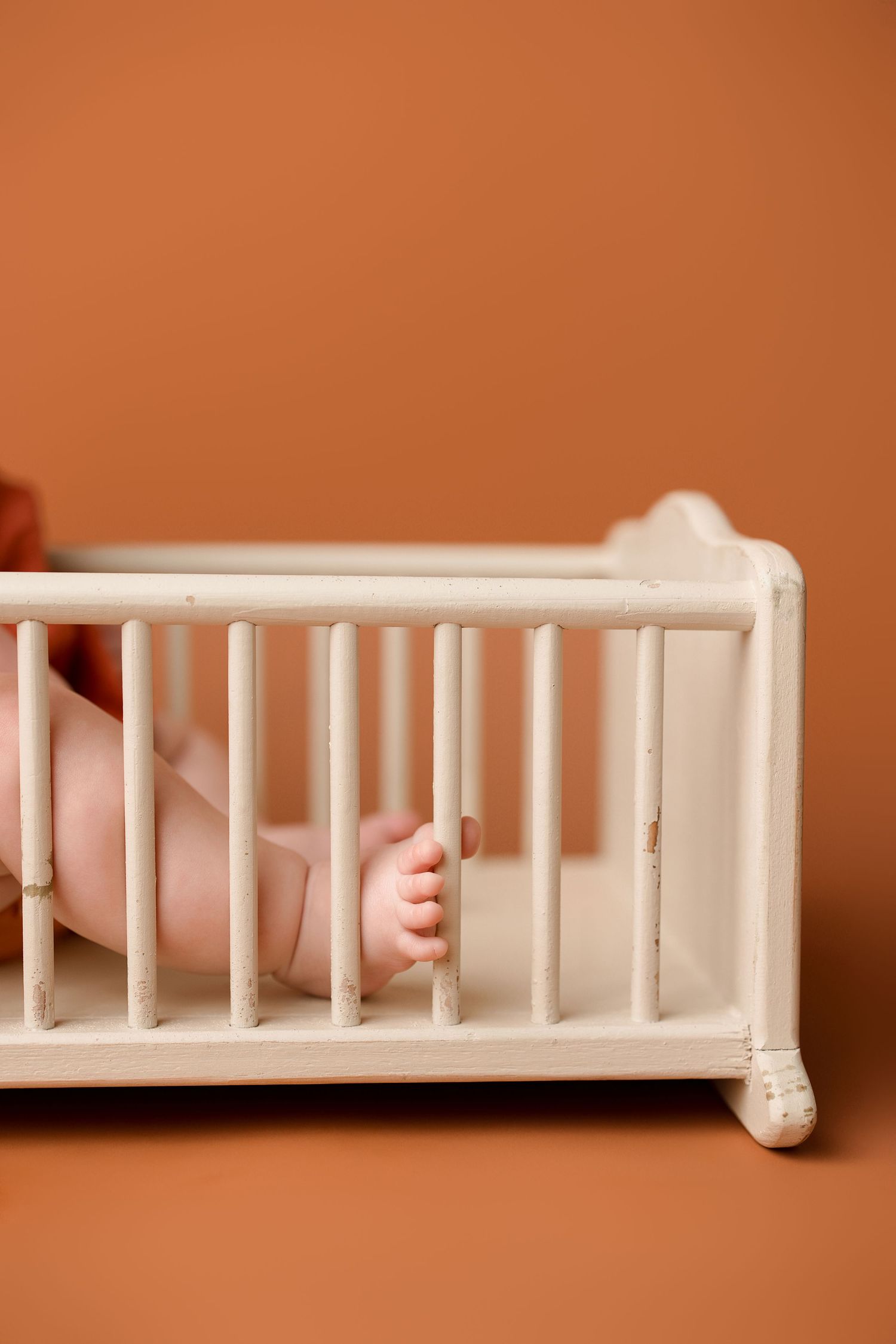A sequence of five images showing small hands gripping white crib bars against an orange background.