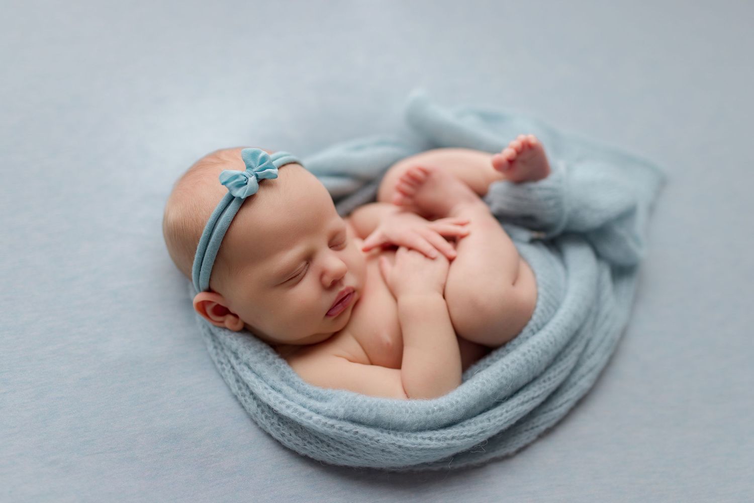 Newborn baby resting on soft blue blanket during professional photo session.