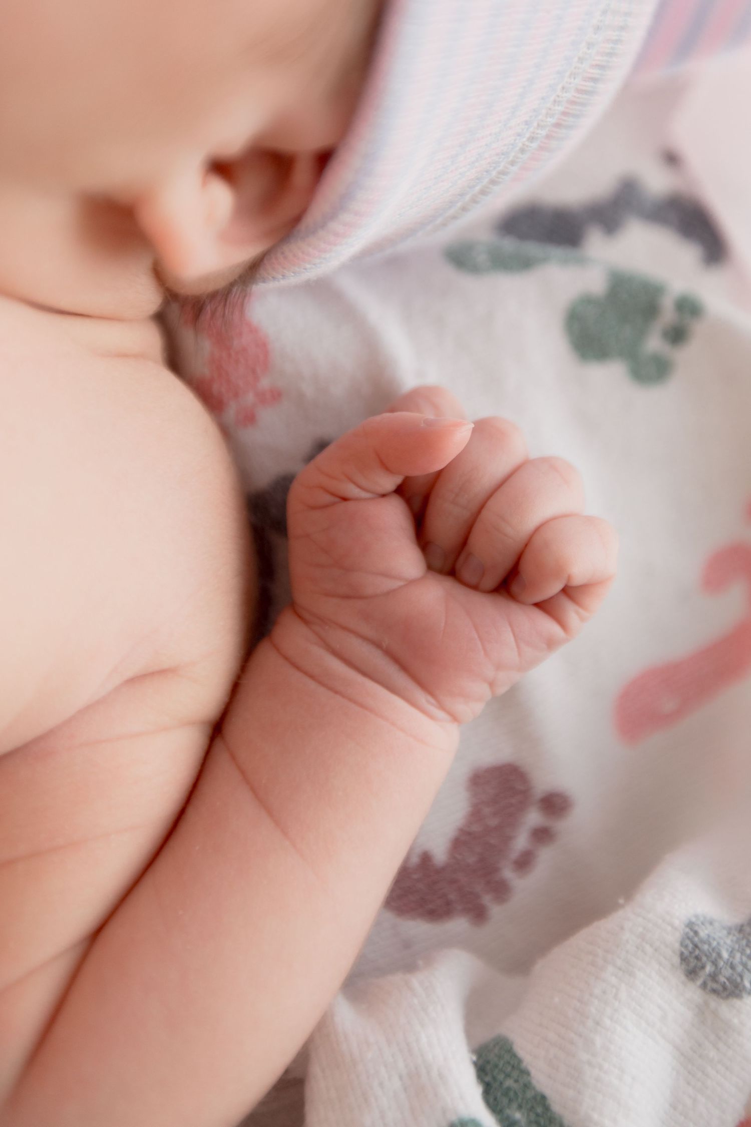 Close-up of tiny newborn baby hand grasping soft patterned blanket with pink and gray designs.