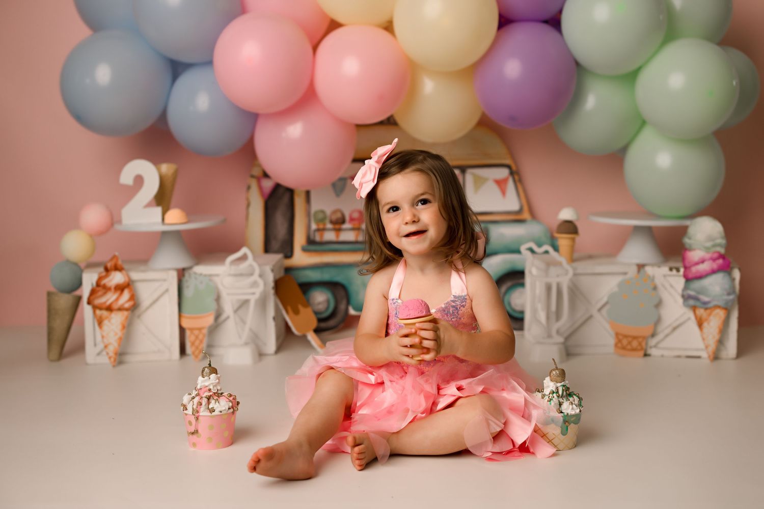 Pastel balloon backdrop with birthday setup featuring ice cream themed decorations.