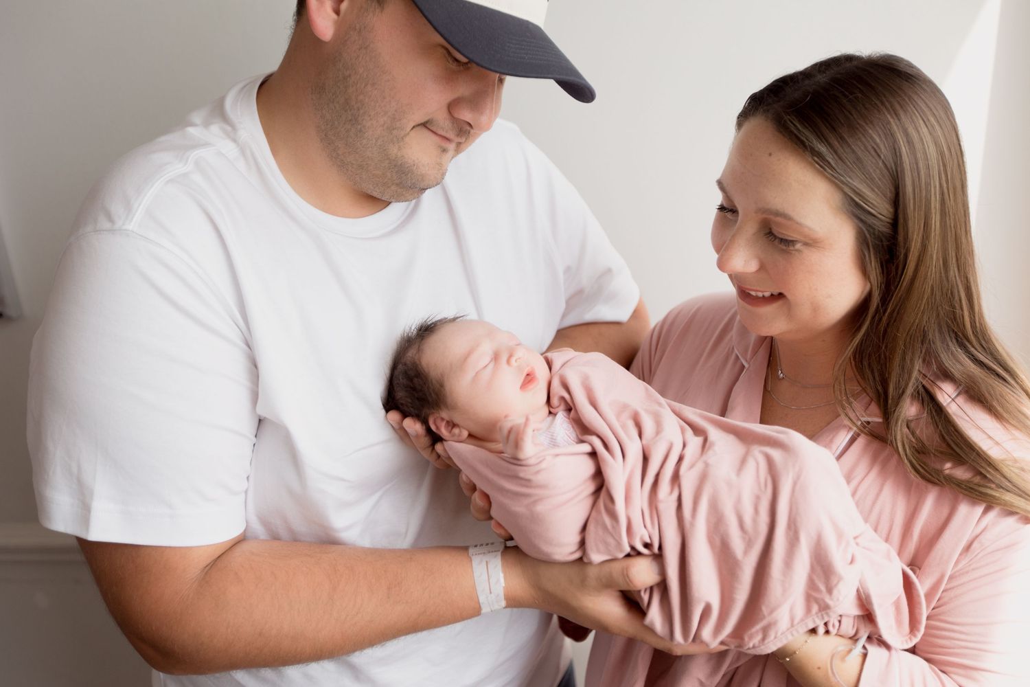 Tender family moment as parents share loving gazes while holding their sleeping newborn baby in pink clothing during Fresh 48 session.