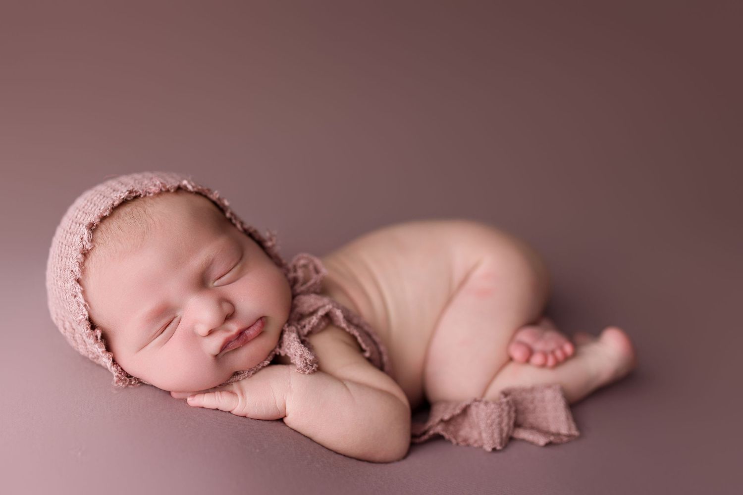 Newborn baby sleeping peacefully on pink blanket in artistic studio photography series.