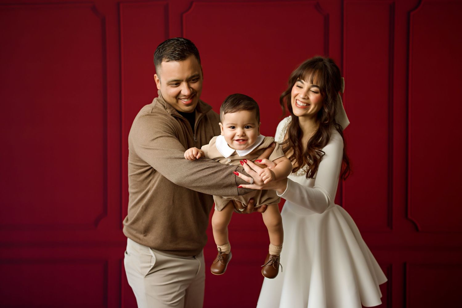 A family in winter attire shares a playful moment against a deep red wall with classic molding.
