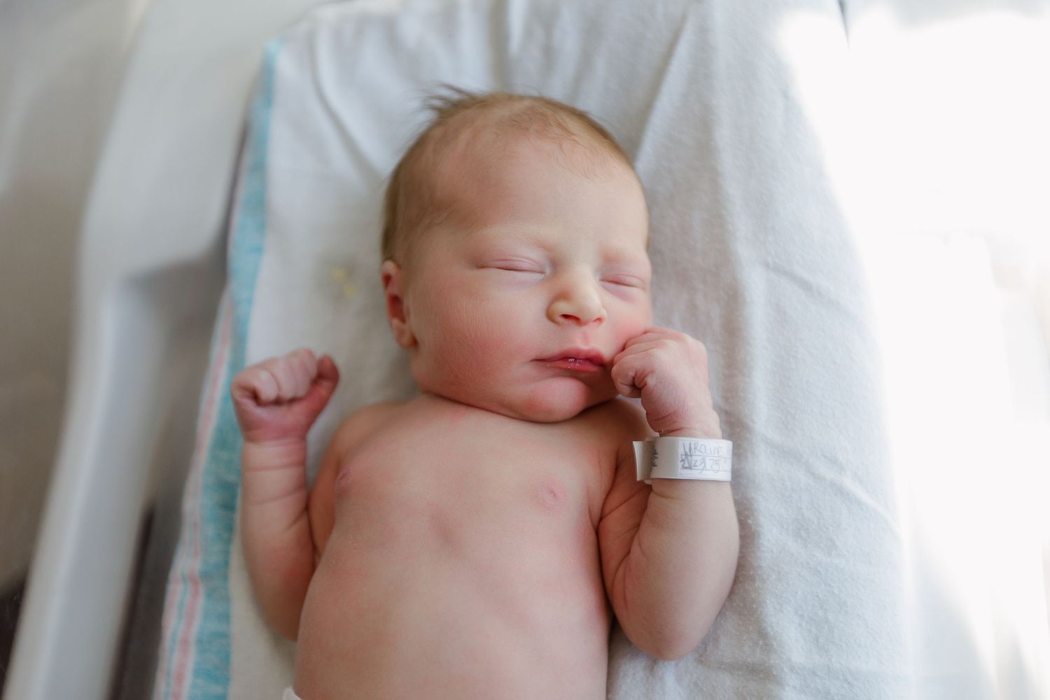 Sleeping newborn swaddled in white blanket against light background during Fresh 48 session in Beaumont hospital.