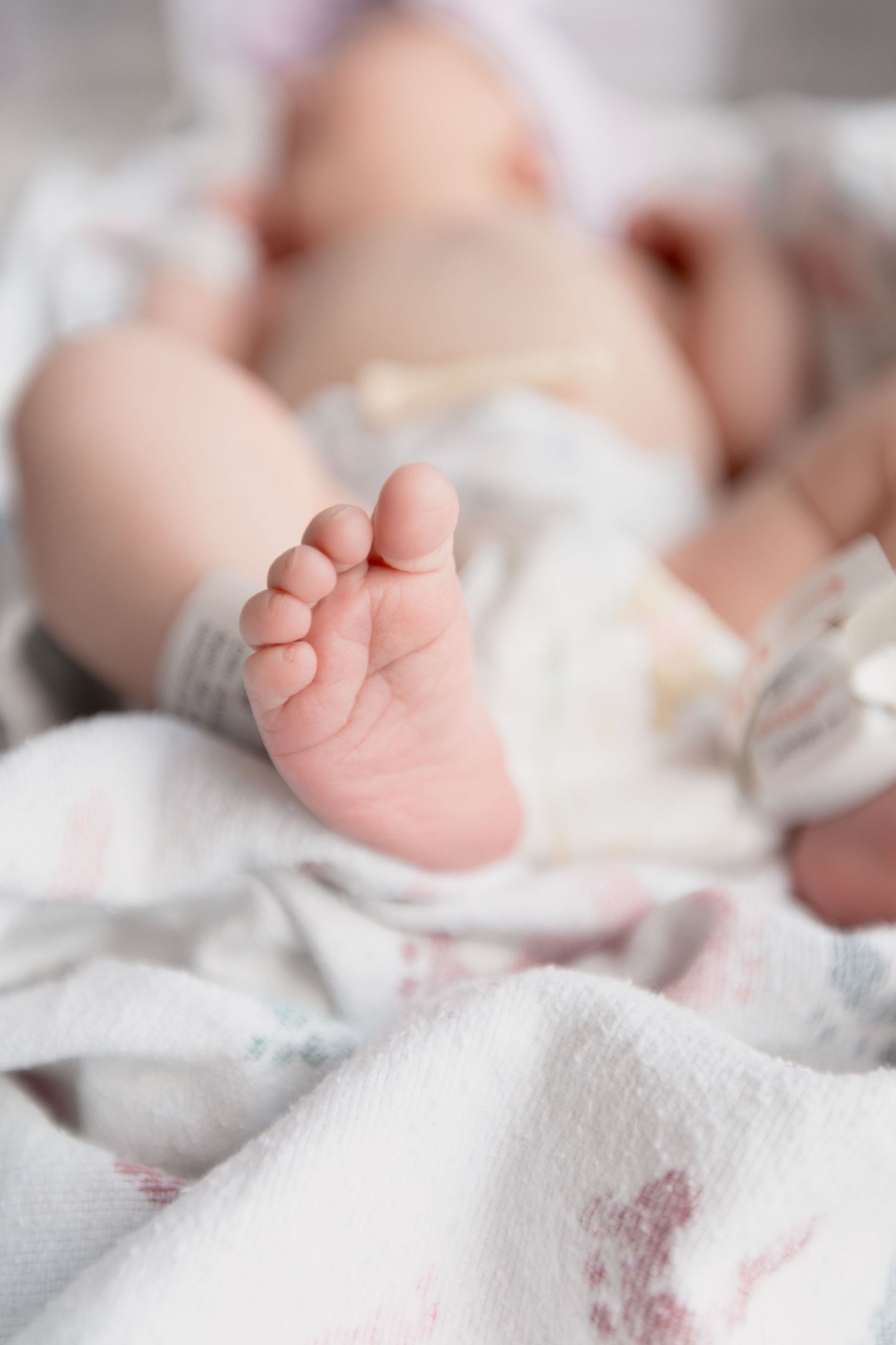 Close-up view of tiny newborn baby feet wrapped in soft white blankets with delicate details.