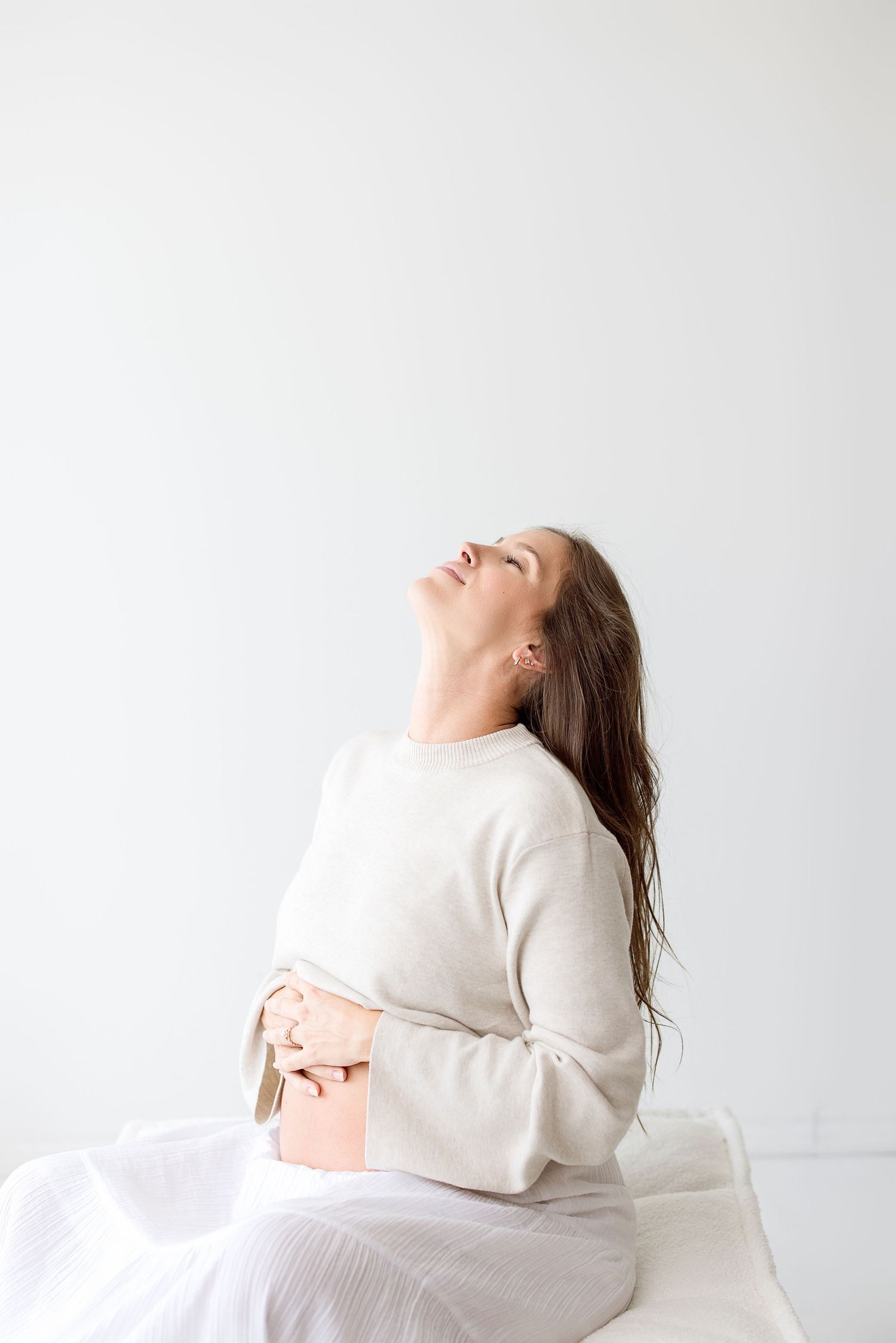 A person in a white sweater sits against a light background with their head tilted back in relaxation.