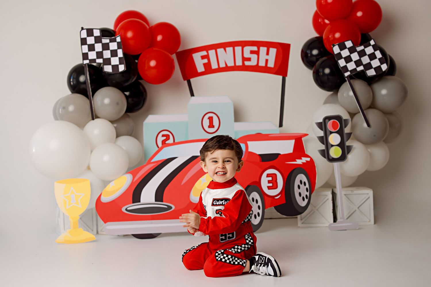 Race car themed photo setup with checkered balloons and red finish line decorations.