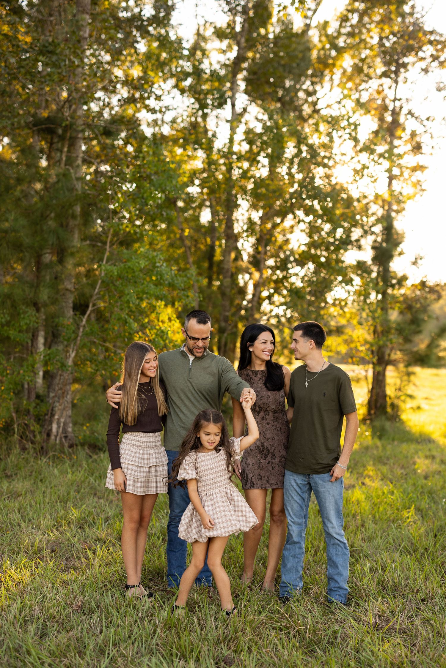 A family walks together through a sunlit wooded area during golden hour as warm light filters through the trees.