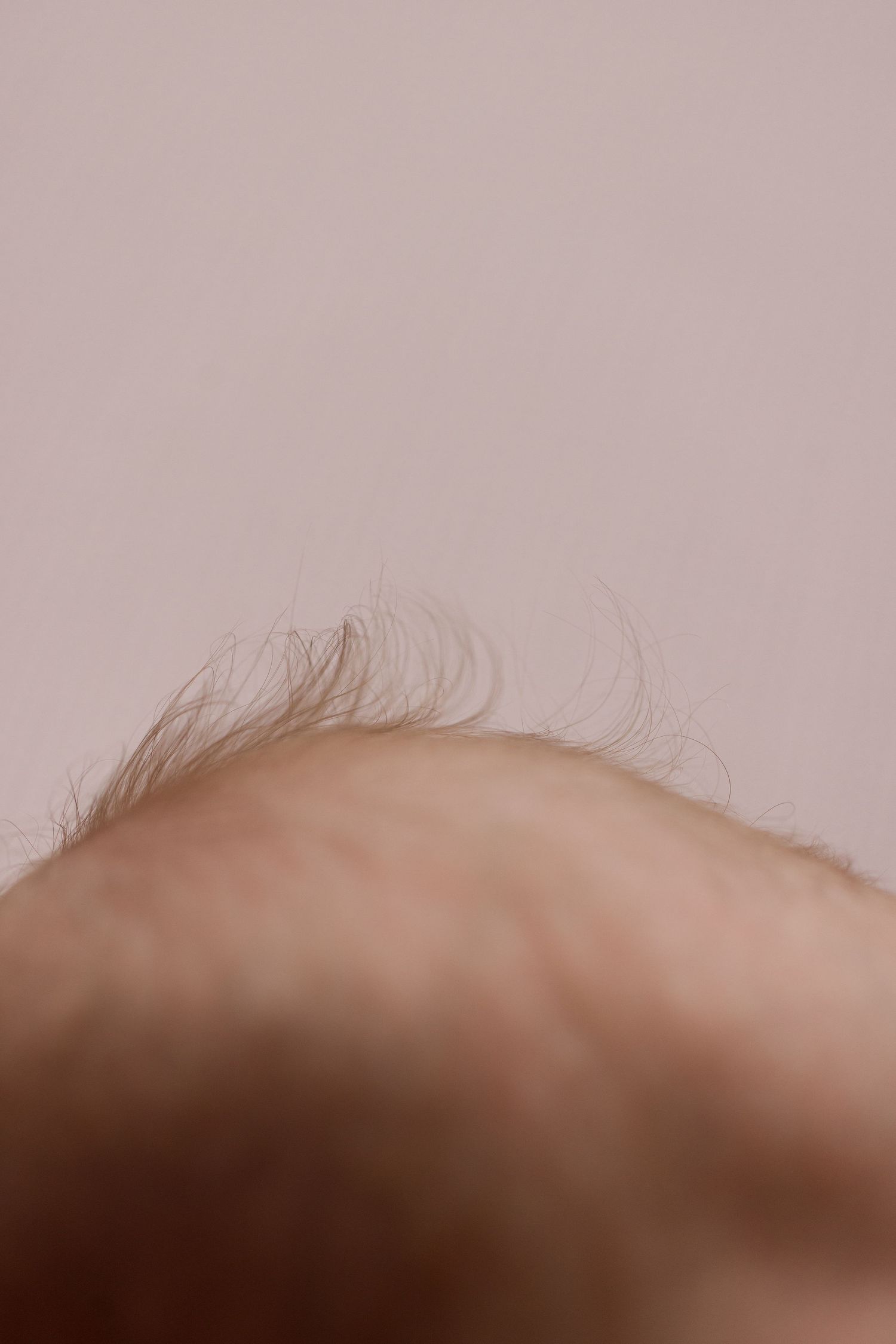 Close-up view of wispy baby hair against a neutral beige background.