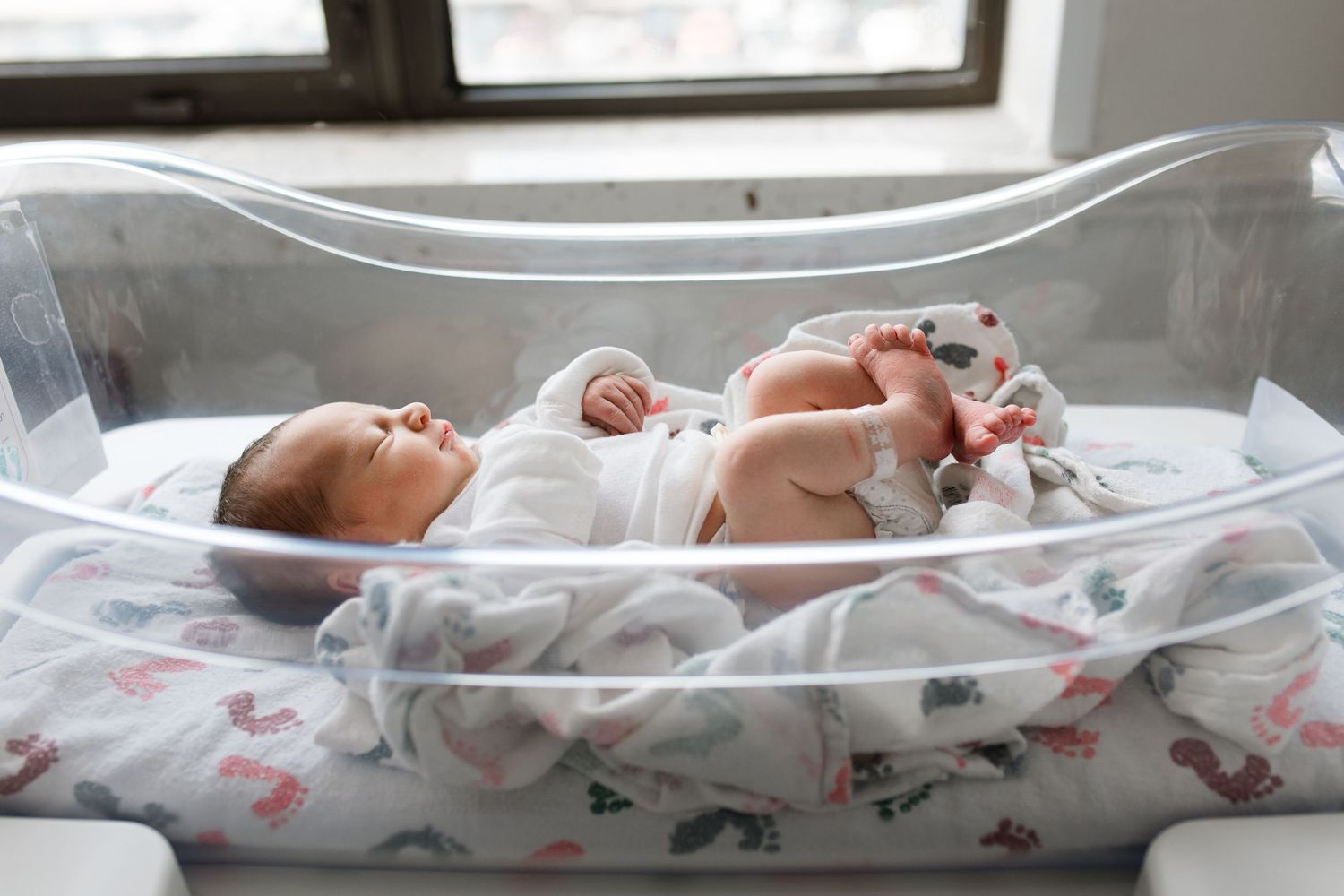 Newborn baby lying in a hospital bassinet, wrapped in a white blanket, peacefully resting after birth.