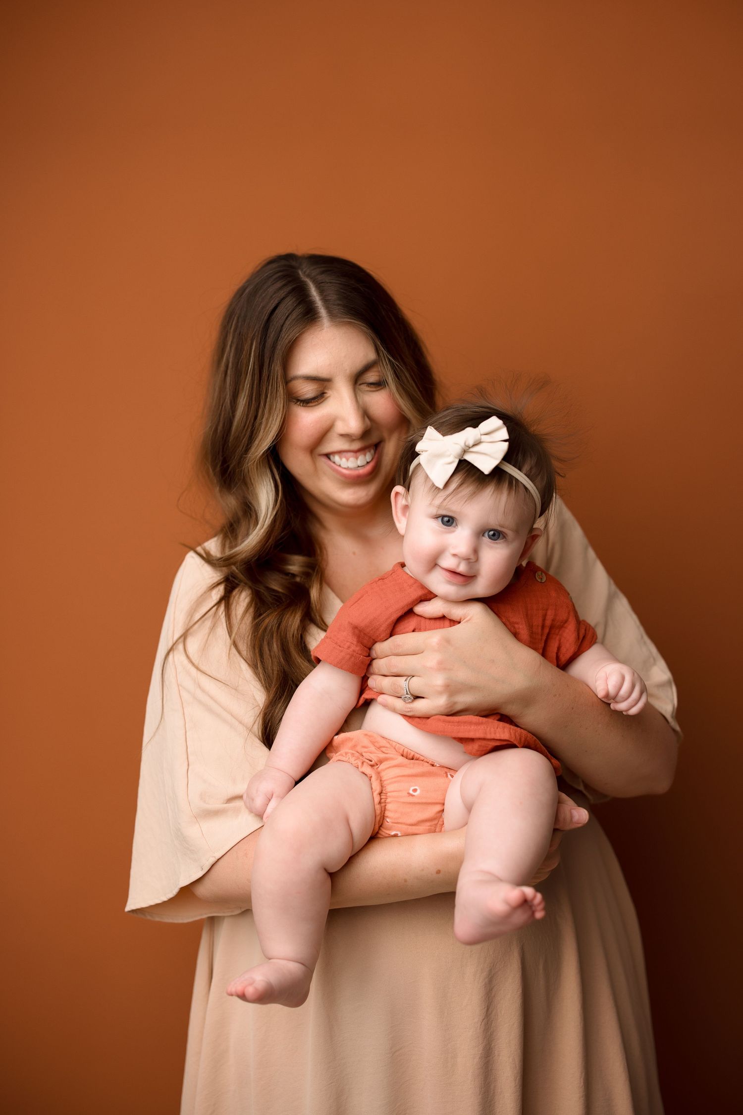 A series of four tender moments between mother and baby in matching peach outfits against a warm brown backdrop.