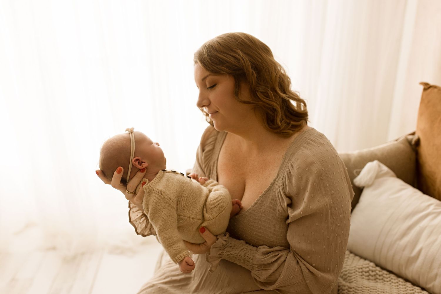 A person in a beige dress lounges on white bedding in a soft, dreamy boudoir photography setting.