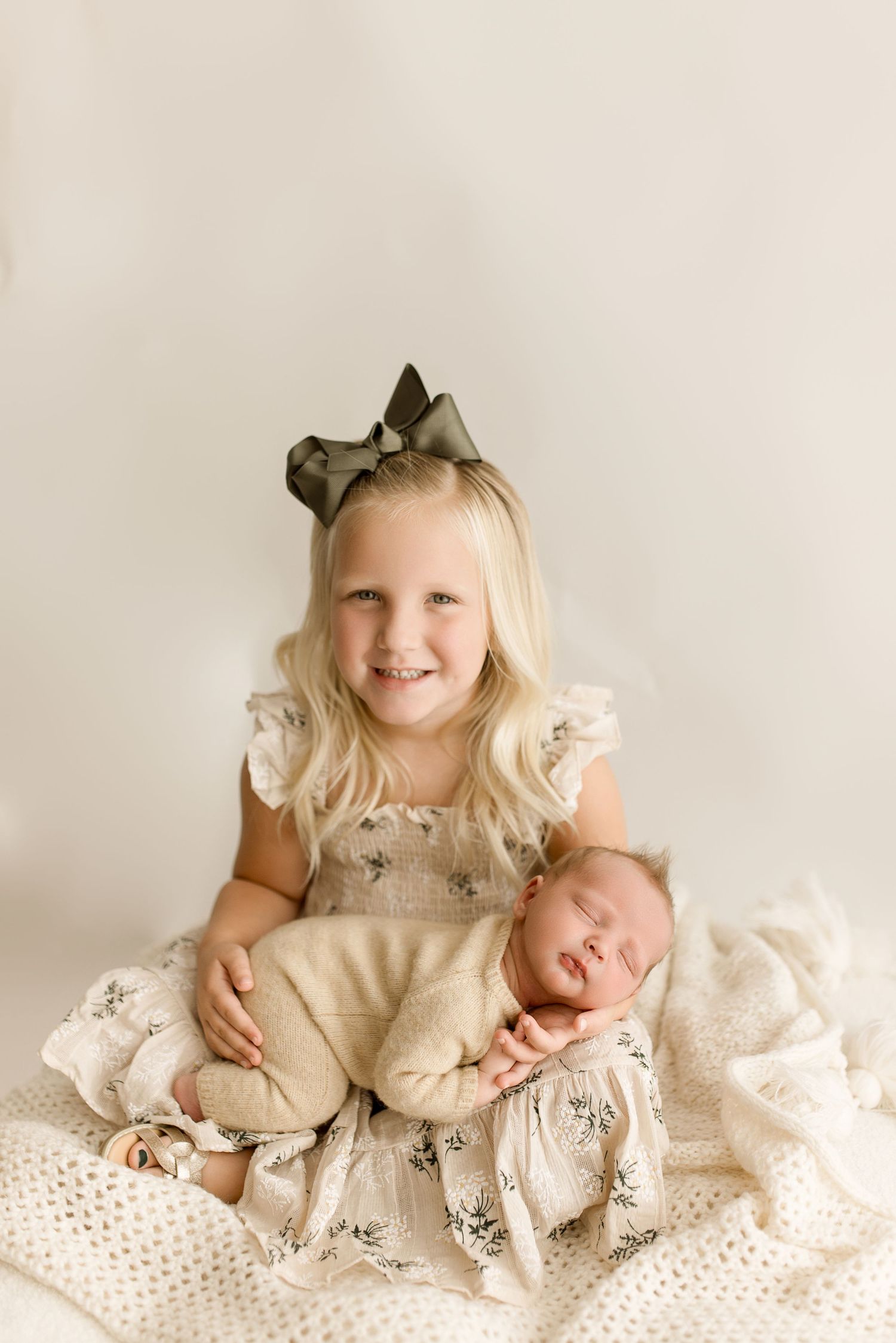 Four progressive images showing a baby and child in vintage-style cream dresses on white textured blankets.