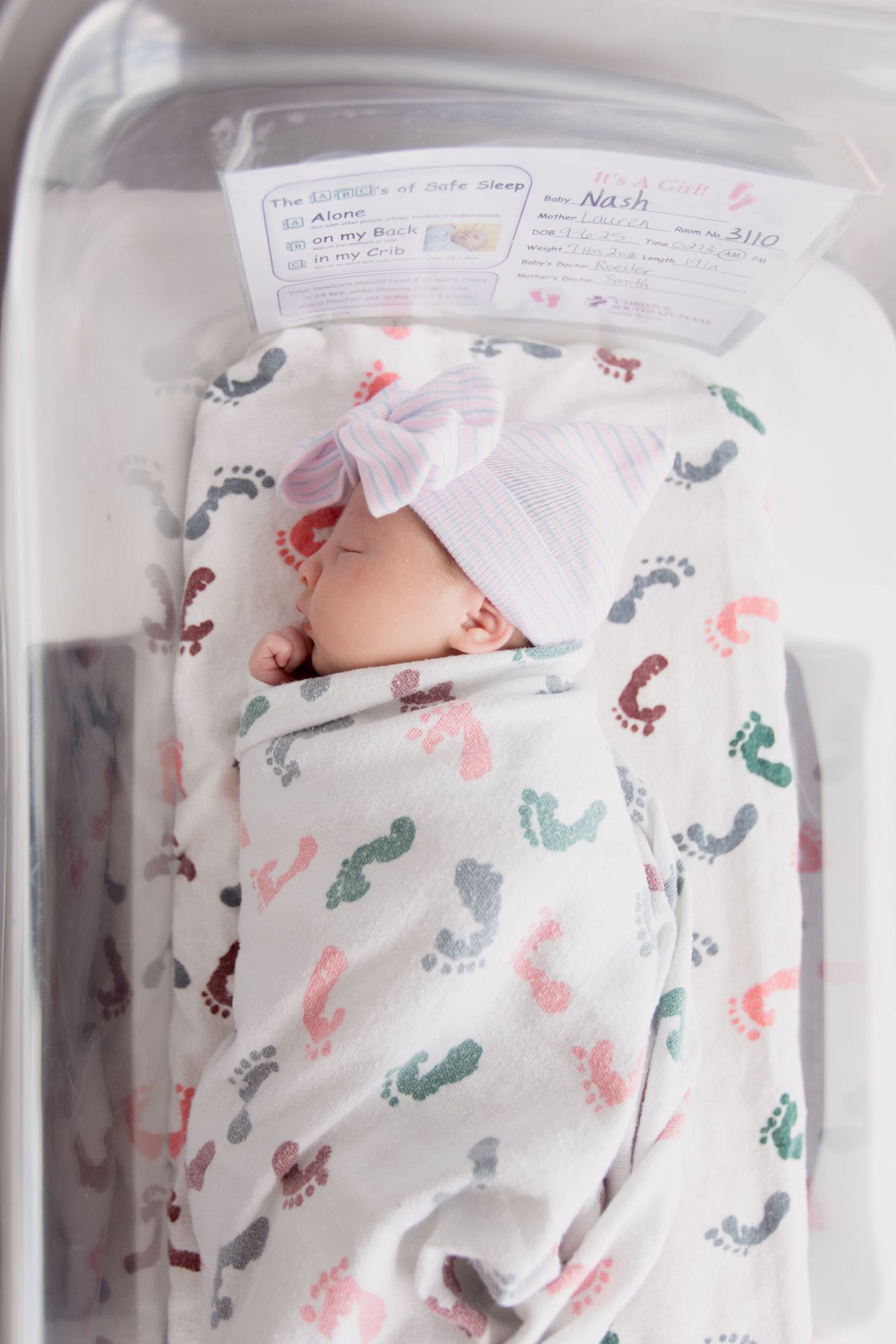 Newborn baby sleeping peacefully on white patterned blanket with footprint designs.