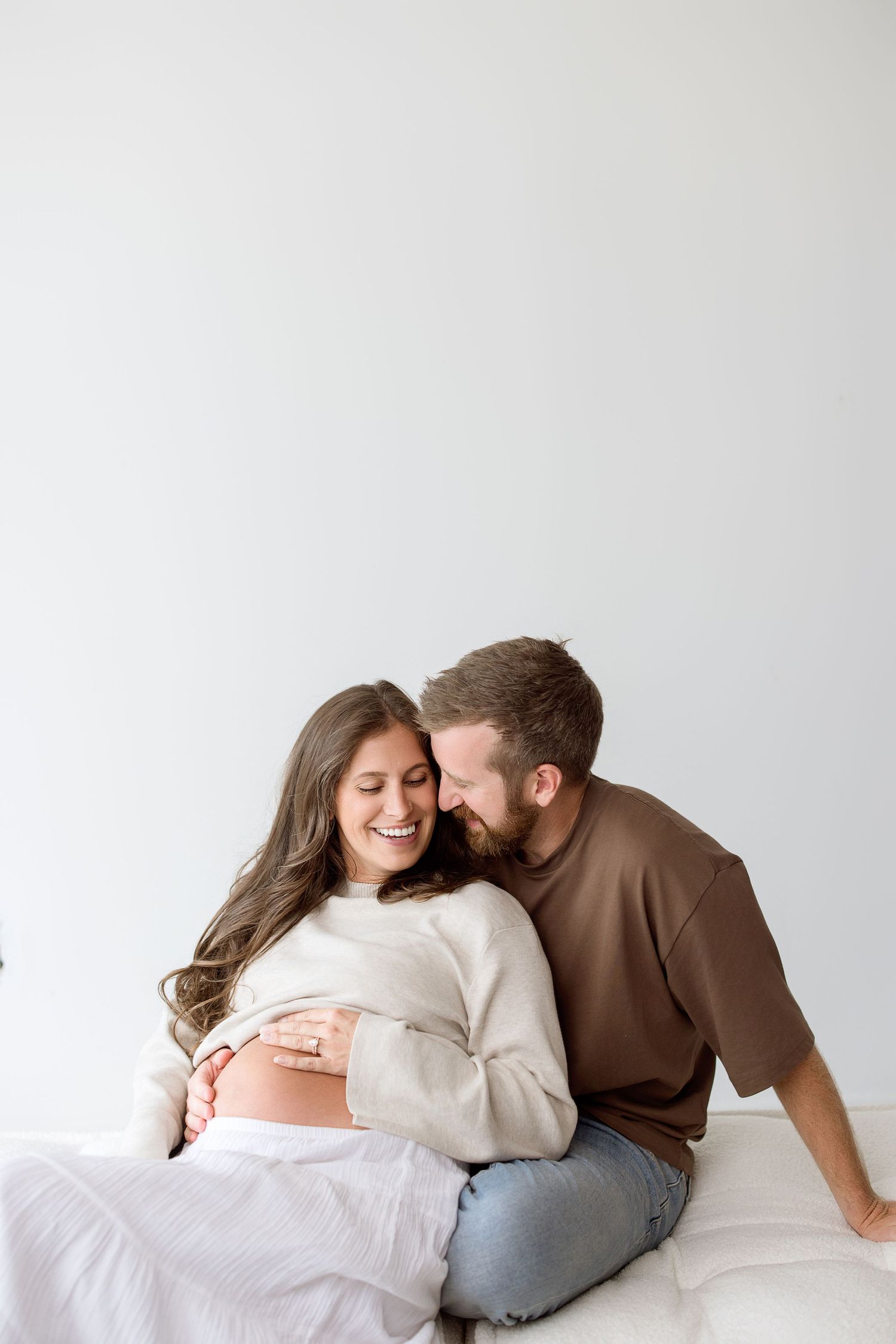 Monochromatic photo series showing intimate moments between expectant couple lying together on white backdrop.