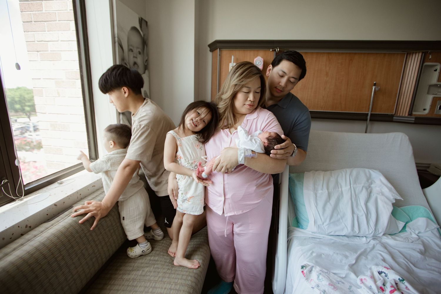 Family gathering by window in hospital room with newborn.