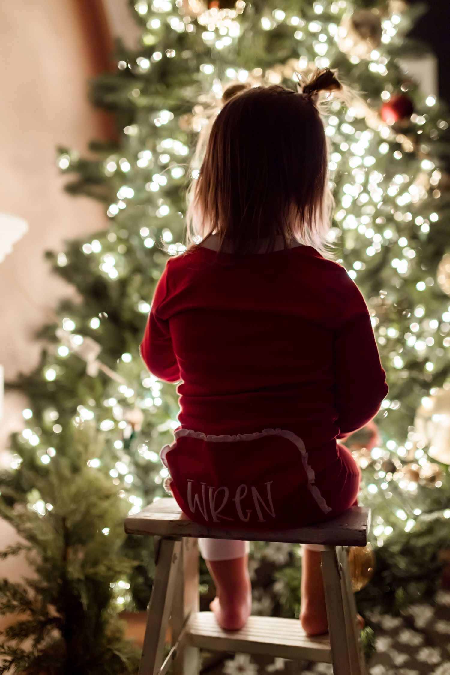 Silhouette of a child in red sitting on a stool looking at a lit Christmas tree.
