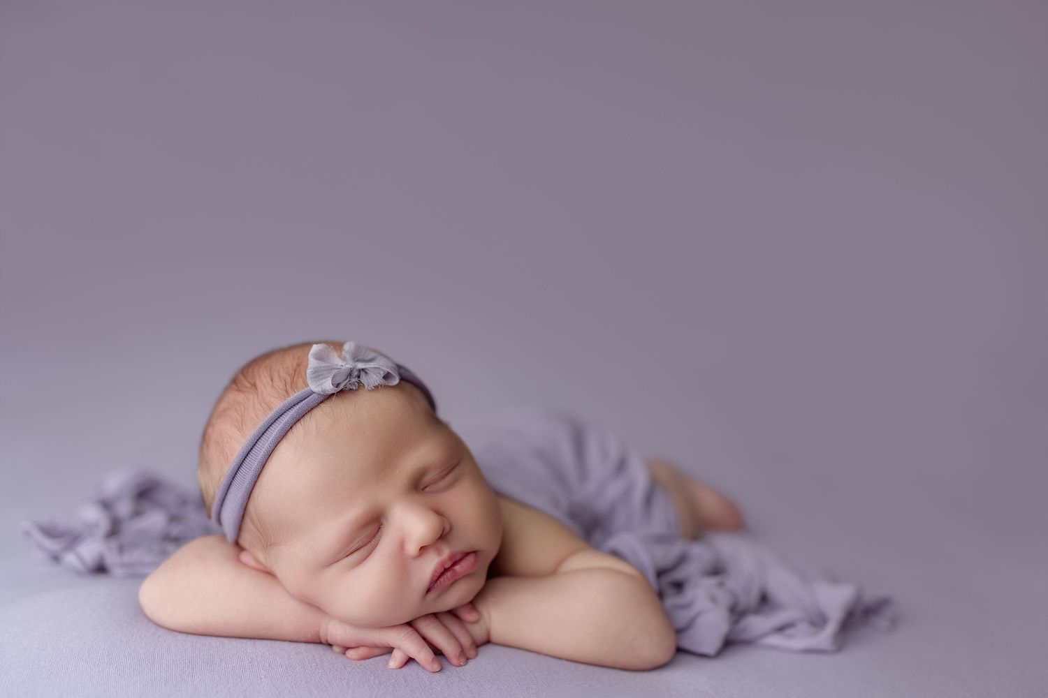 Newborn baby peacefully sleeping on soft purple blanket in professional studio setting.